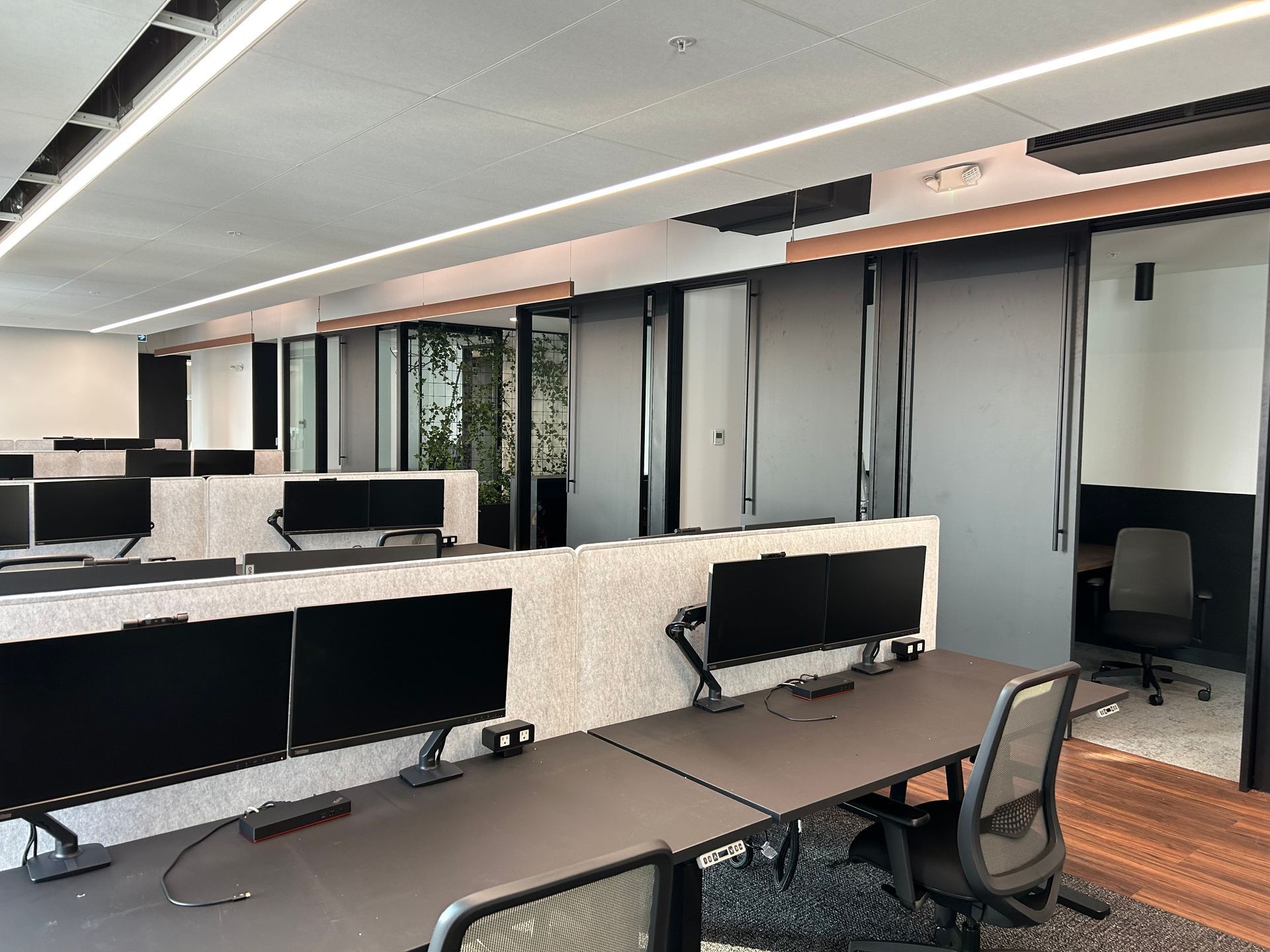 Espace de travail de bureau avec des rangées d'écrans d'ordinateur sur les bureaux, et des bureaux privés en arrière-plan.