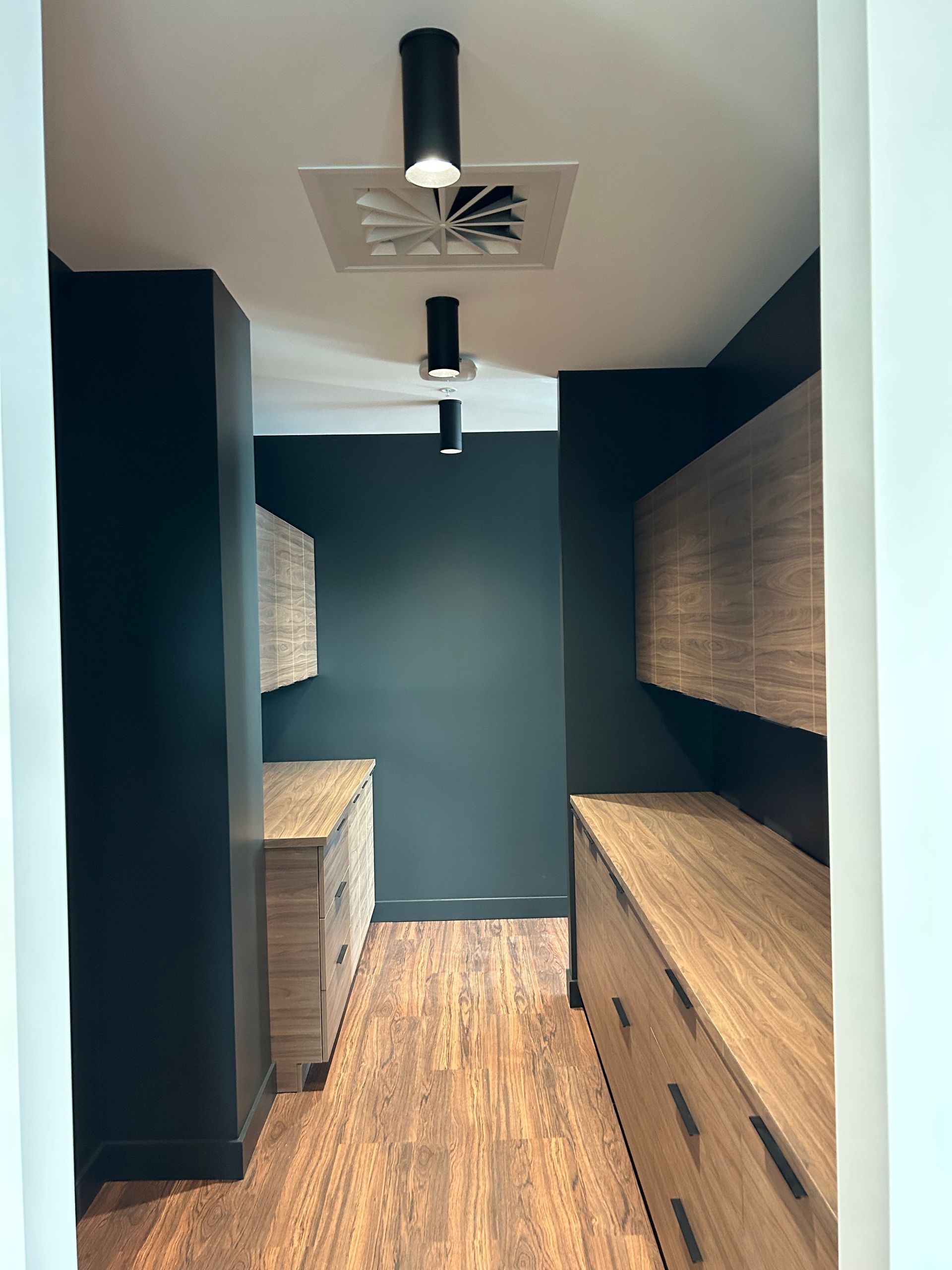Un couloir étroit aux murs sombres, avec des meubles en bois et des spots encastrés.