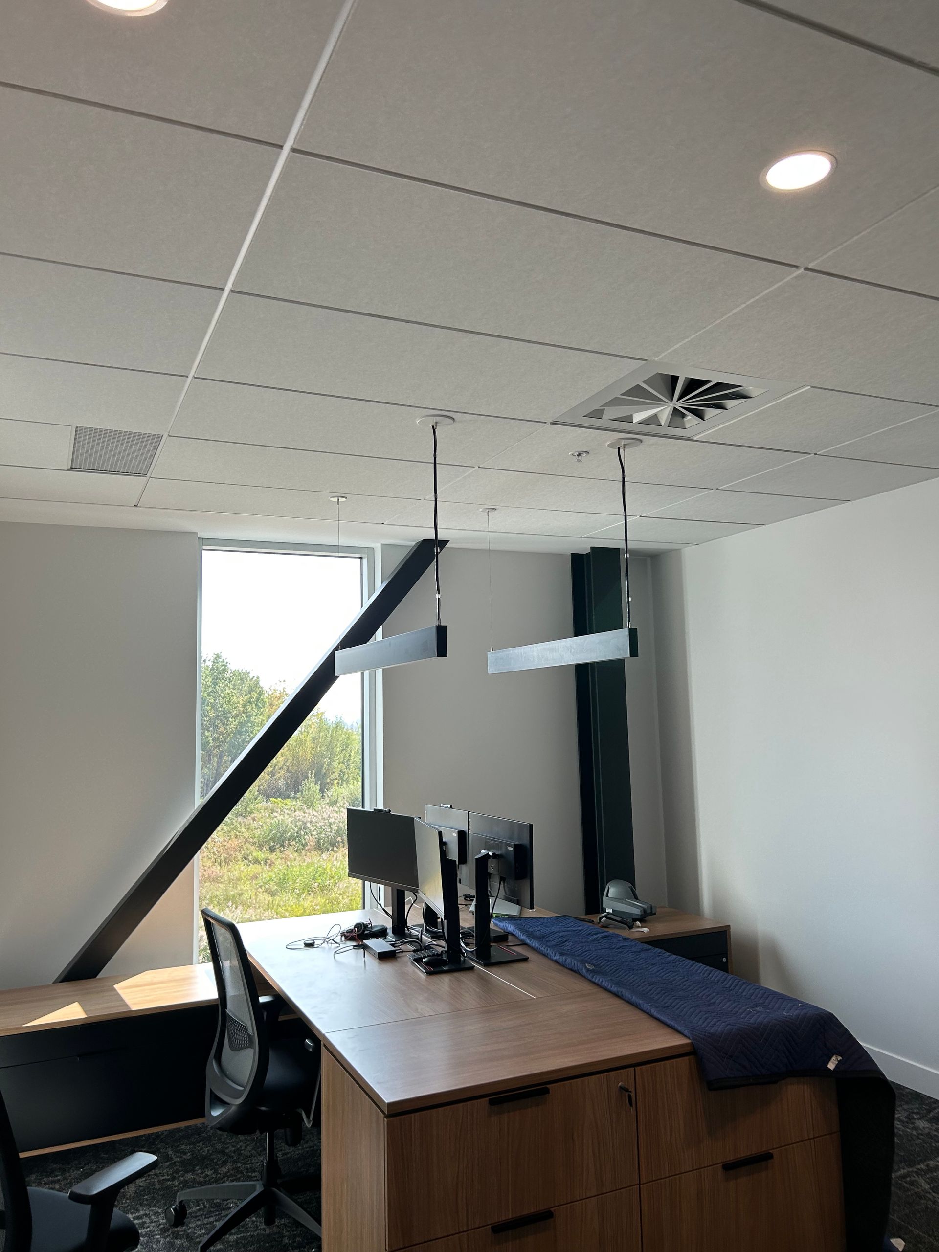 Intérieur de bureau avec bureau, fenêtre, éclairage au plafond et poutre structurelle inclinée.
