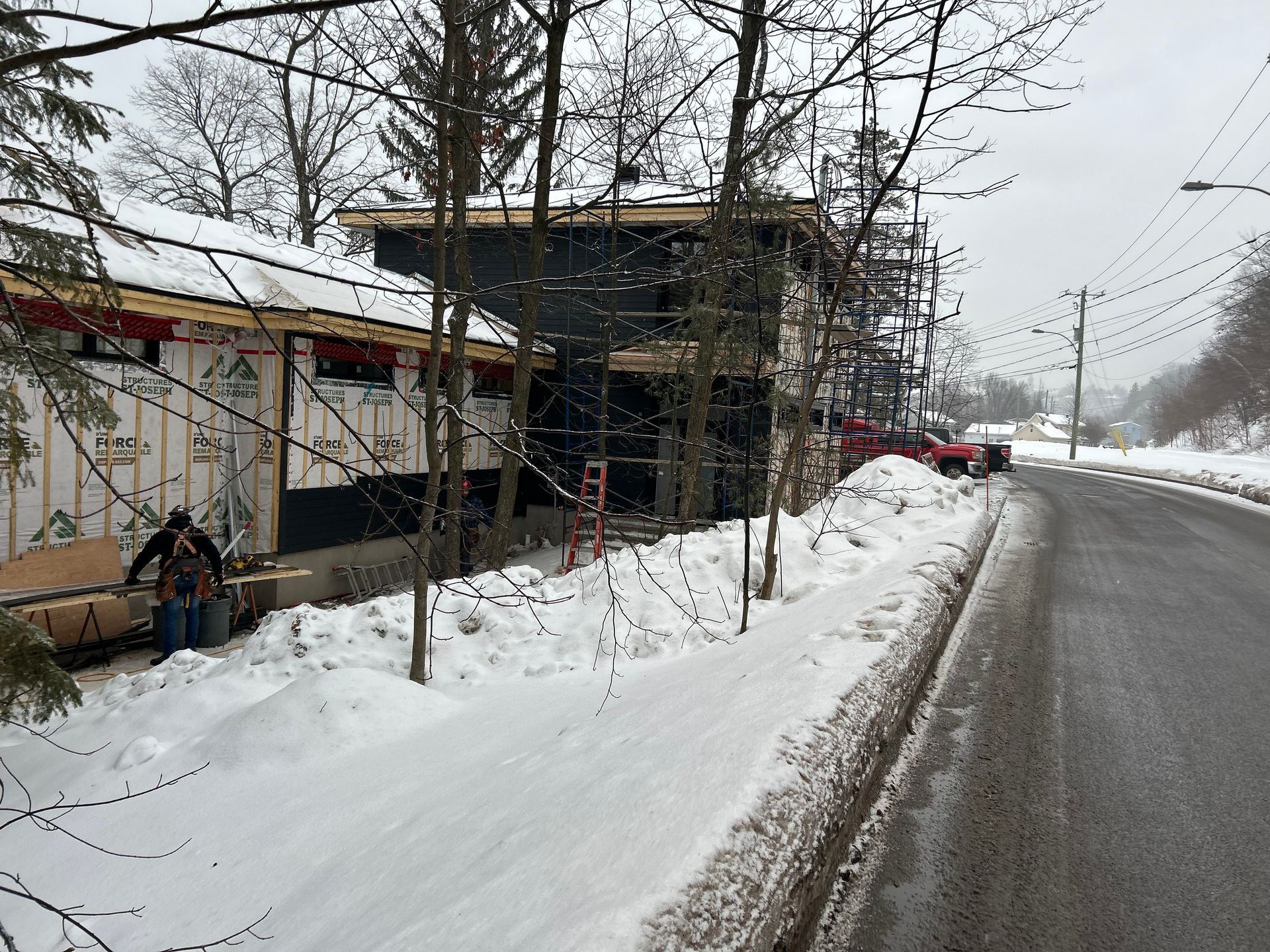 Chantier de construction avec sol enneigé et un bâtiment entouré d'échafaudages. Une personne travaille sur la façade