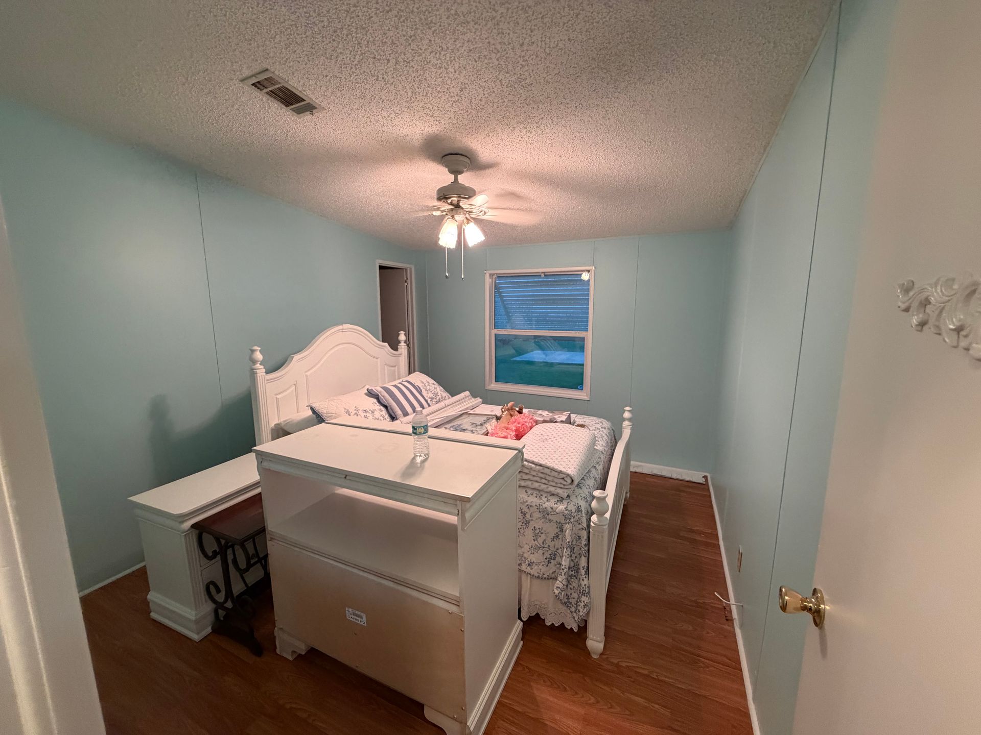 Small bedroom with a bed, white dresser, blue walls, wood floor, and ceiling fan.