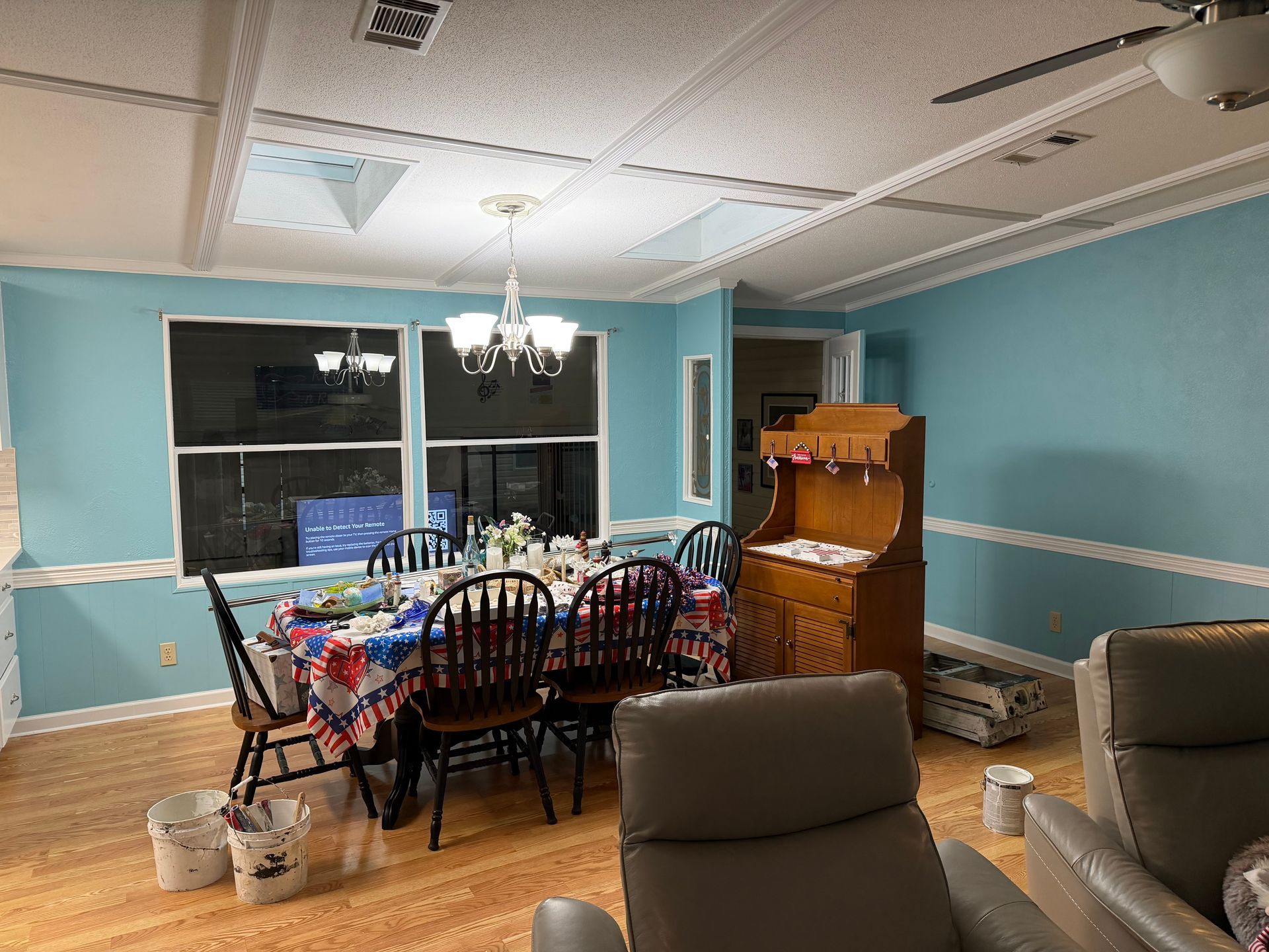 Dining room with blue walls, dark wood table and chairs, chandelier, piano, and recliner in foreground.