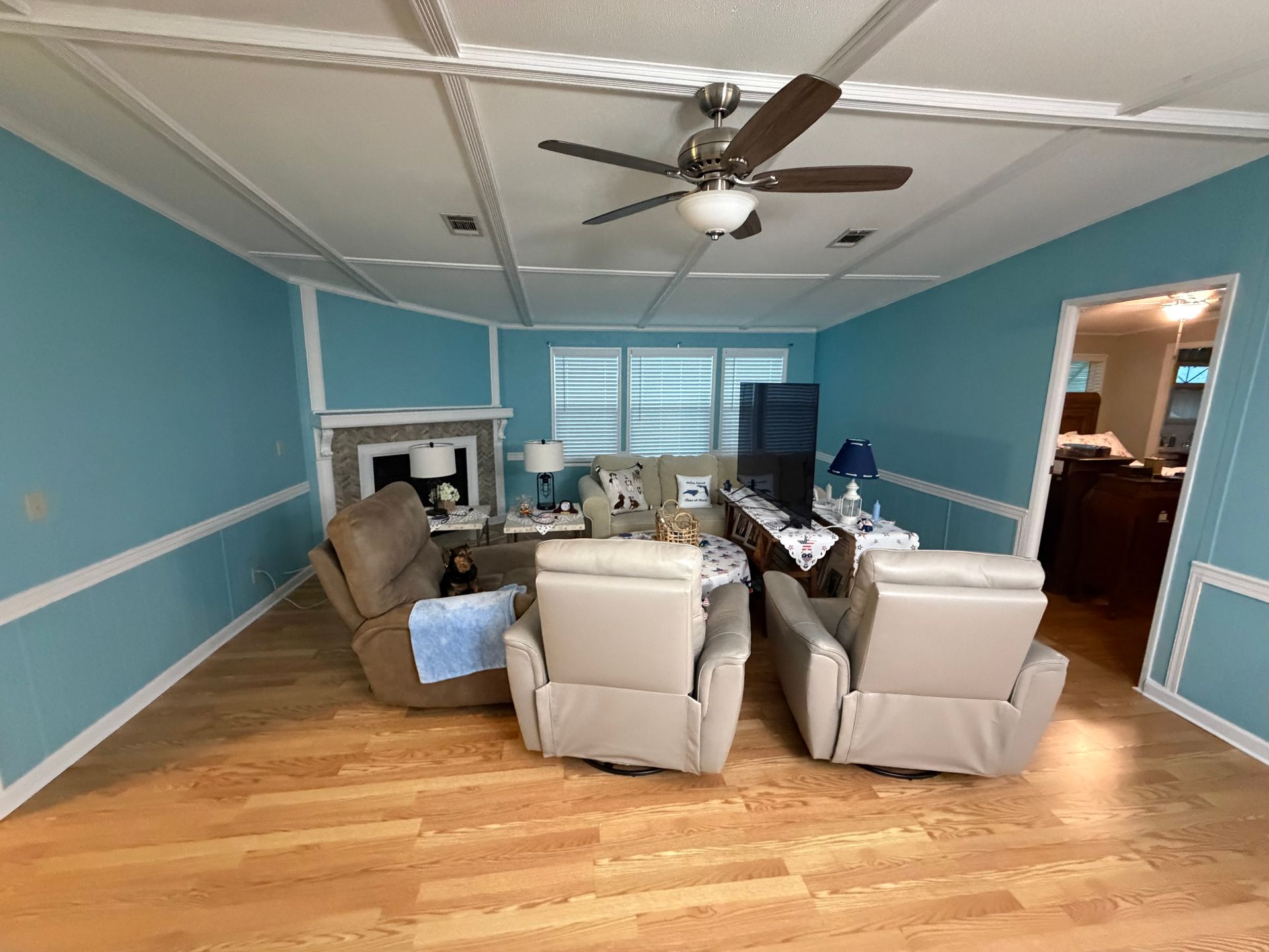 Living room with blue walls, hardwood floor, sectional chairs, and a ceiling fan near a window.