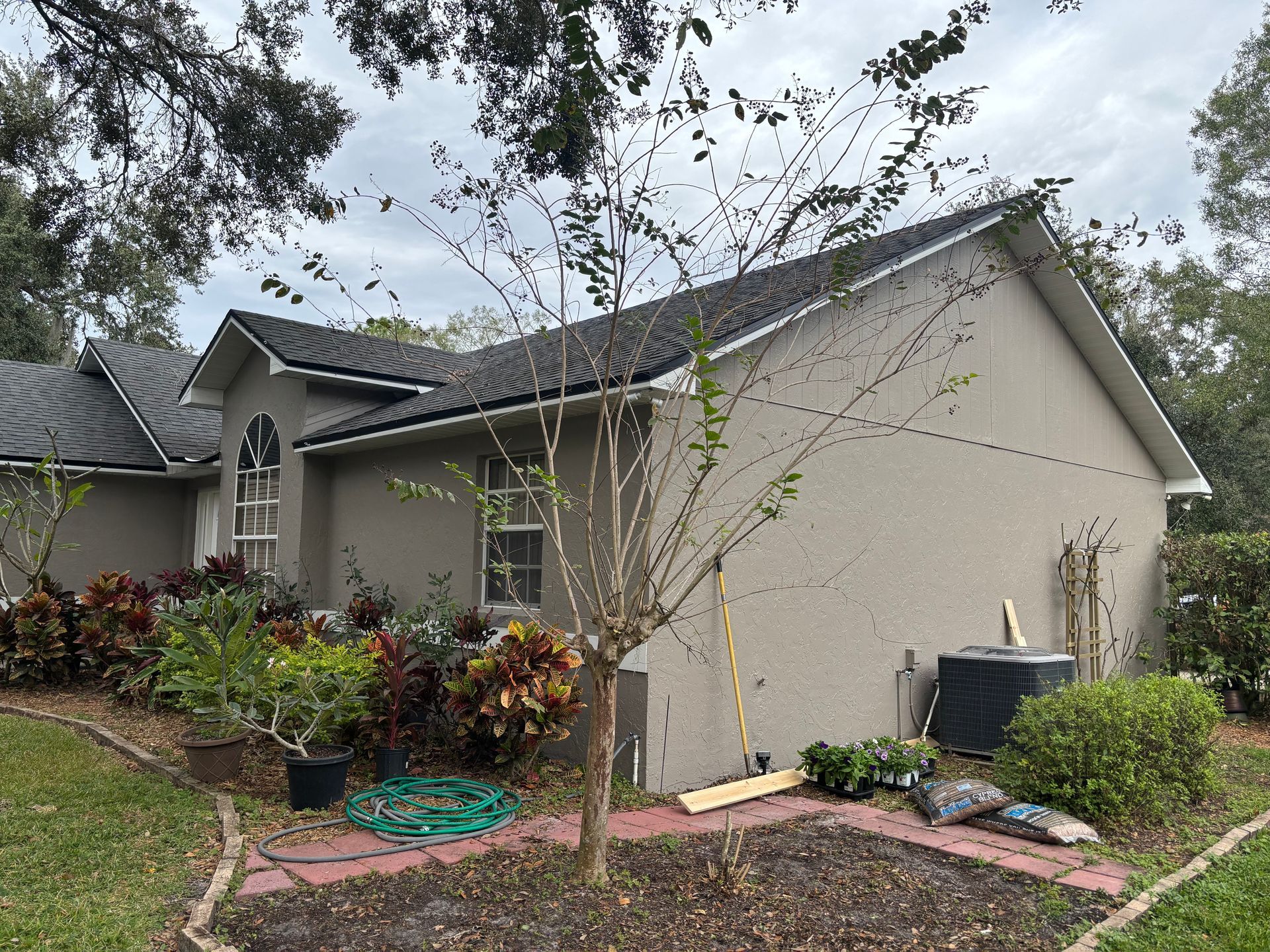House with dark roof, tan siding, and garden in front. Overcast day.