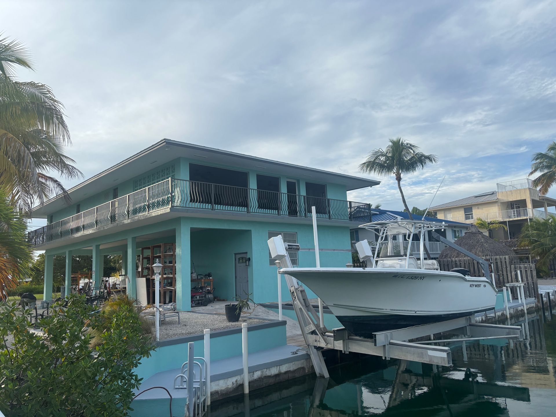 Turquoise waterfront house with a boat docked beside it under a cloudy sky
