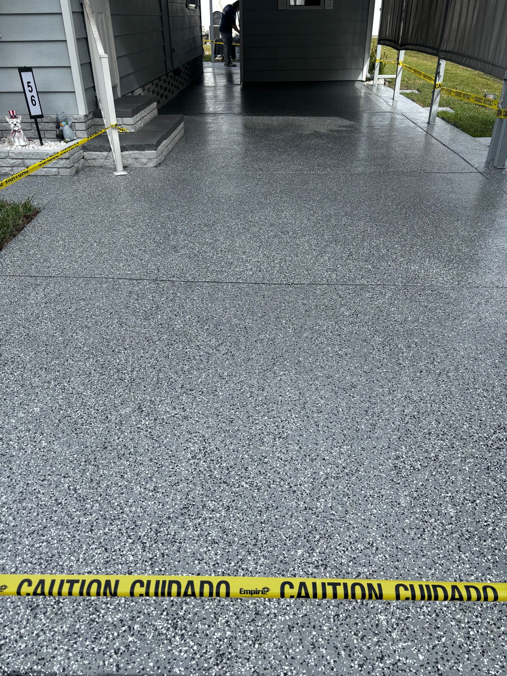 Caution tape blocking a wet speckled concrete walkway beside a building entrance.
