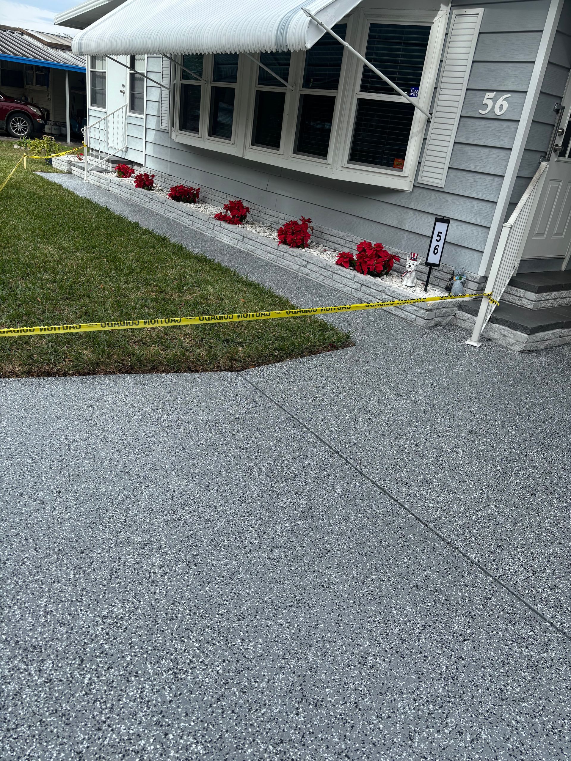 Gray house with white awning, red flowers along the wall, and a yellow rope marking the gravel driveway