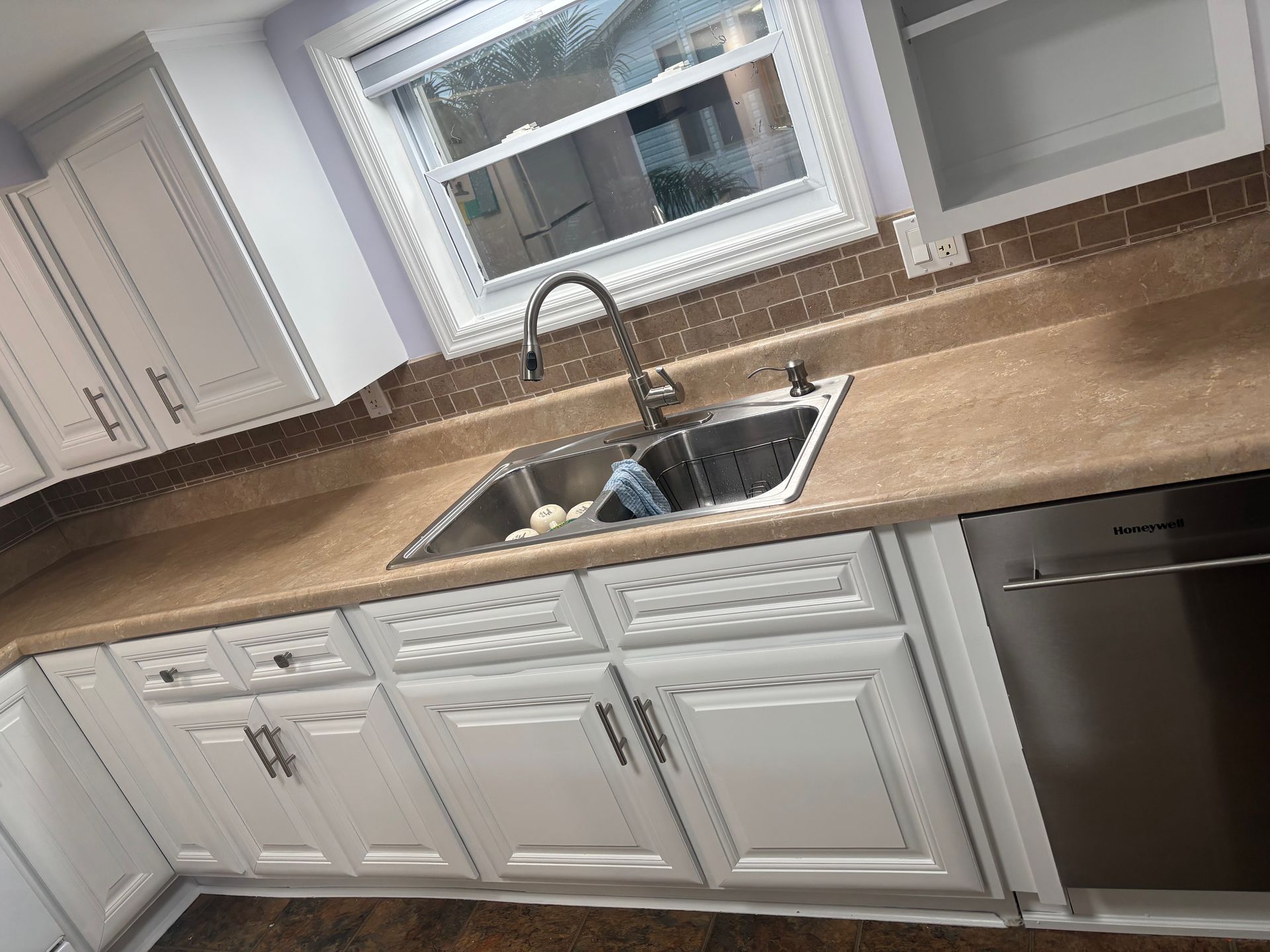 Kitchen sink with white cabinets, beige countertop, and window above the faucet.