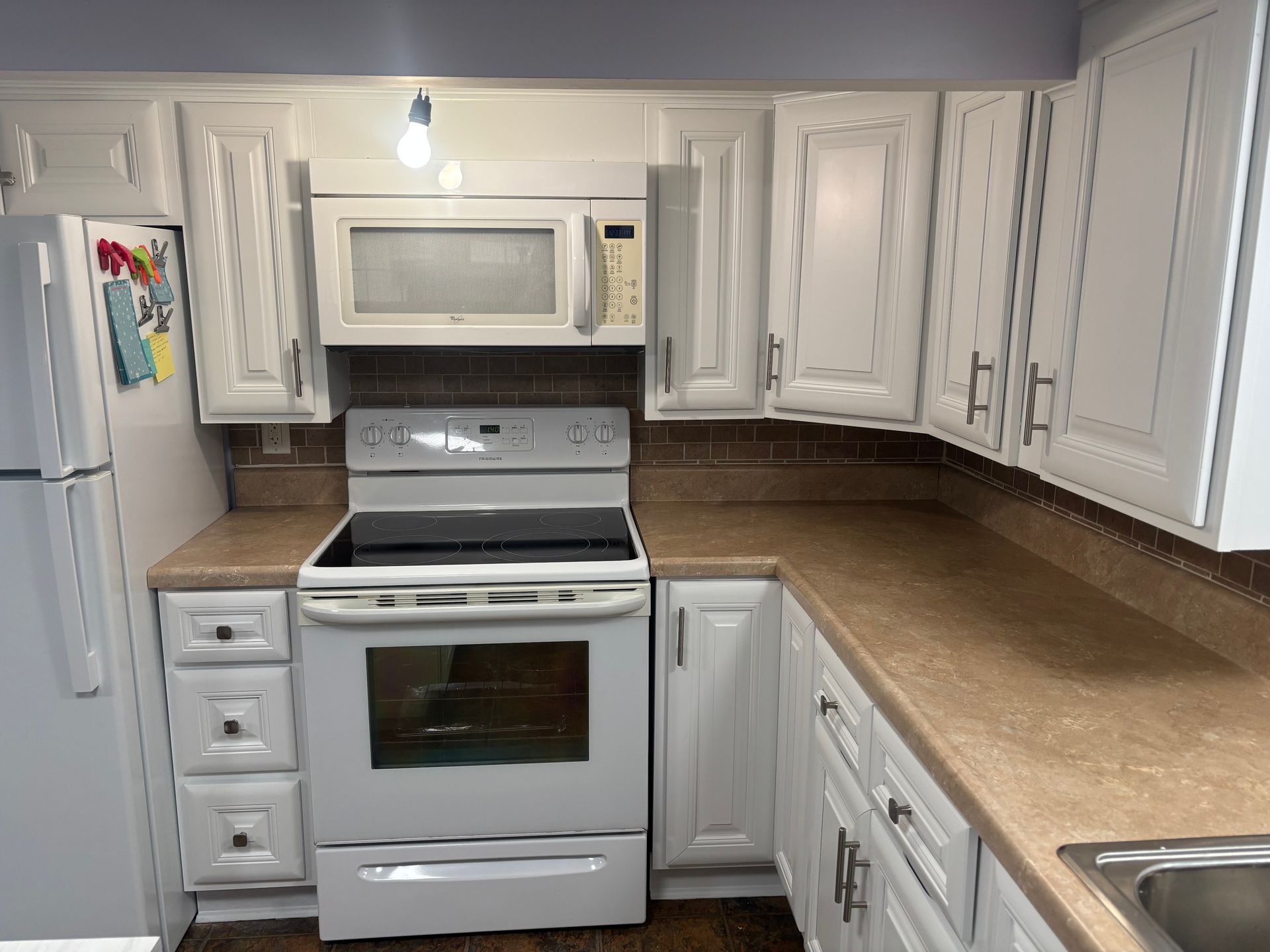 White kitchen with microwave over stove, white cabinets, and tan countertops