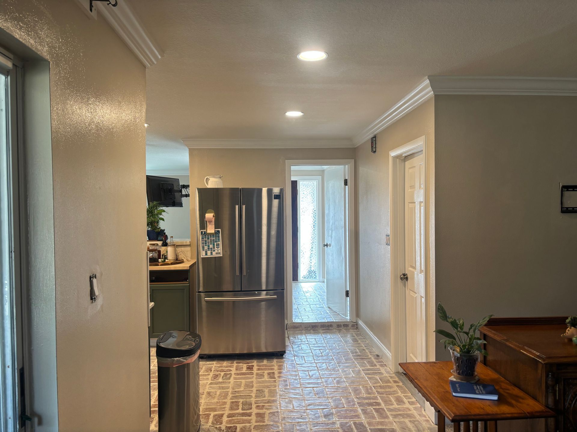 Bright kitchen hallway with stainless steel fridge, tiled floor, and wooden piano at right