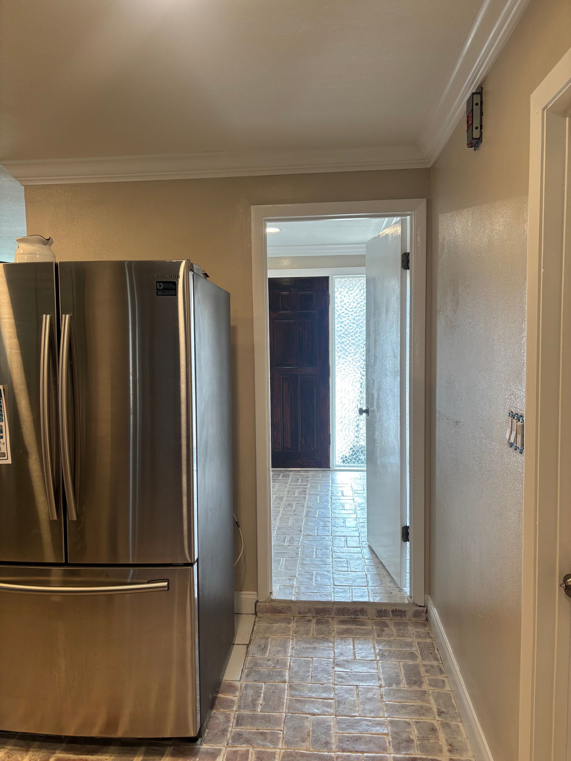Kitchen with stainless steel refrigerator, beige walls, and a tiled floor leading to a doorway.