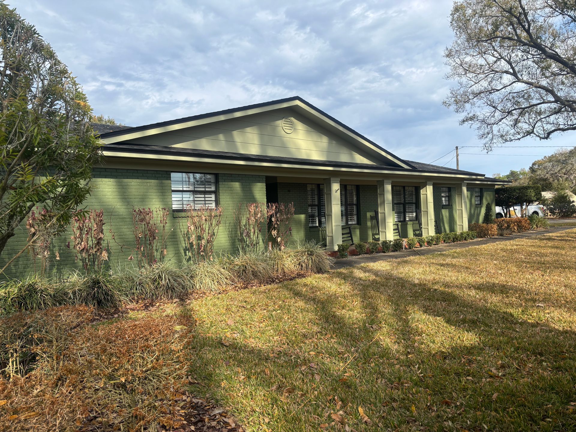 Single-story green house with a front porch and large yard under a cloudy sky