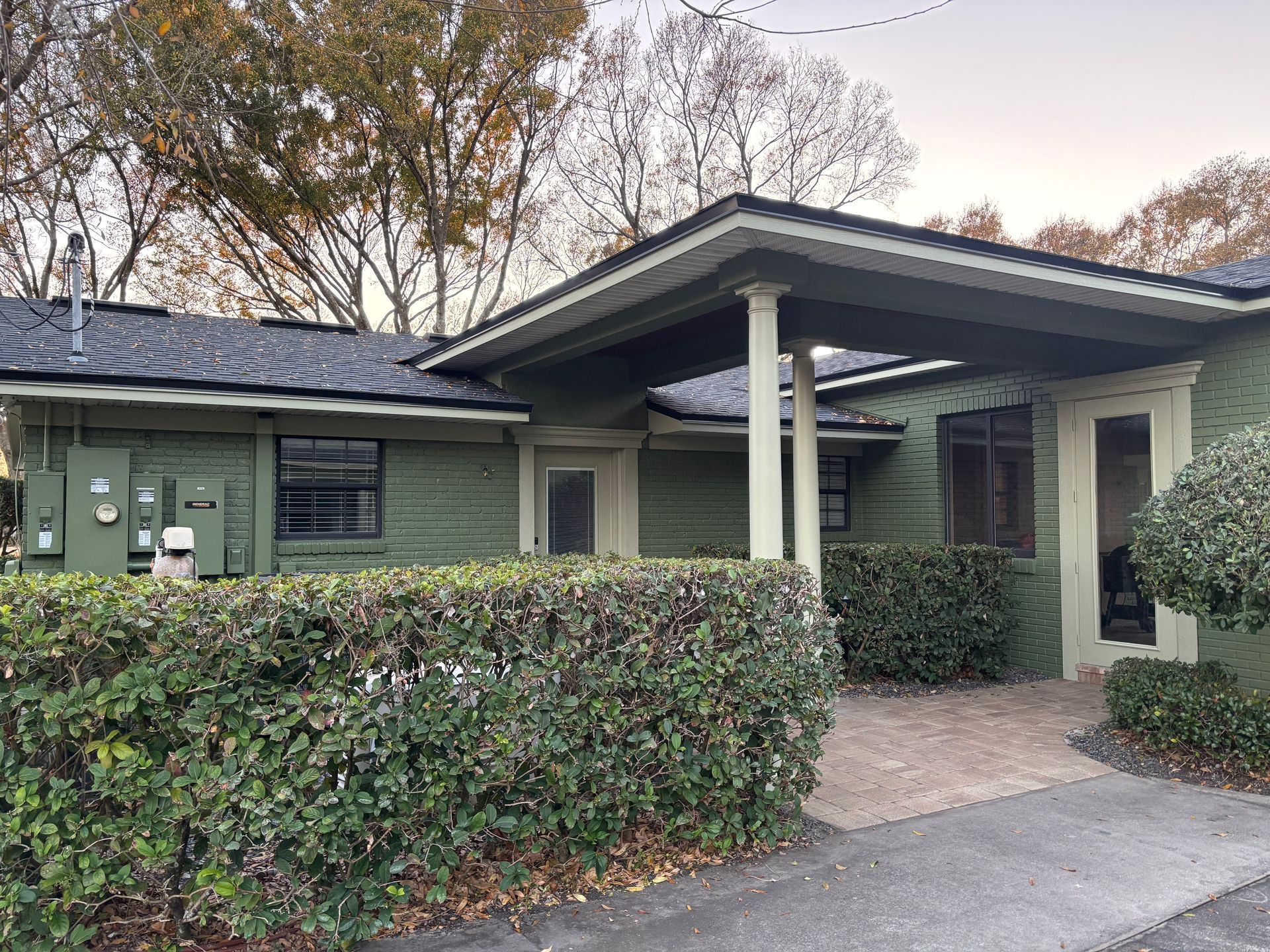 Modern green house entrance with covered porch, hedge, and stone walkway