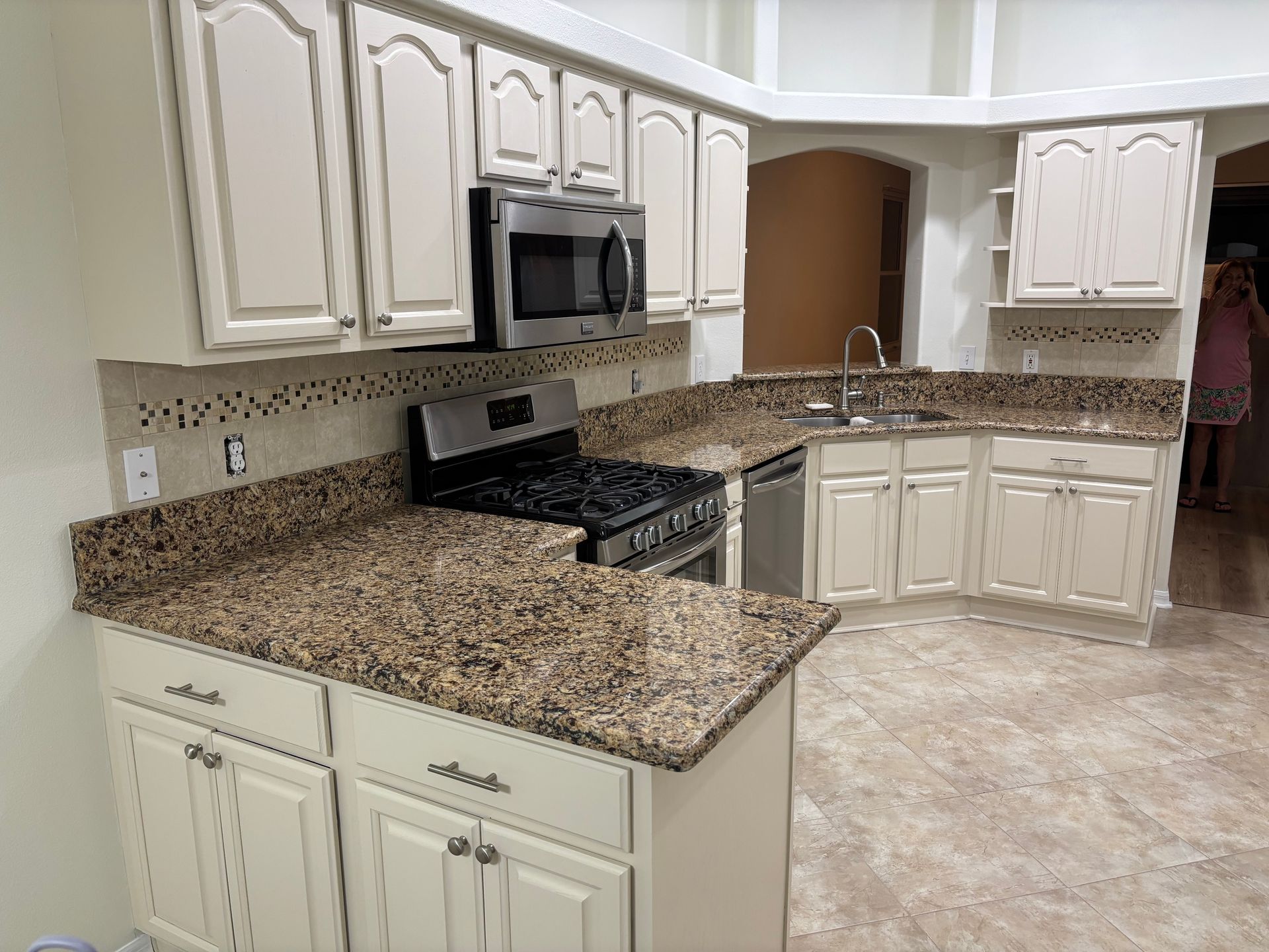 Bright kitchen with cream cabinets, speckled granite counters, stainless stove, and beige tile floor