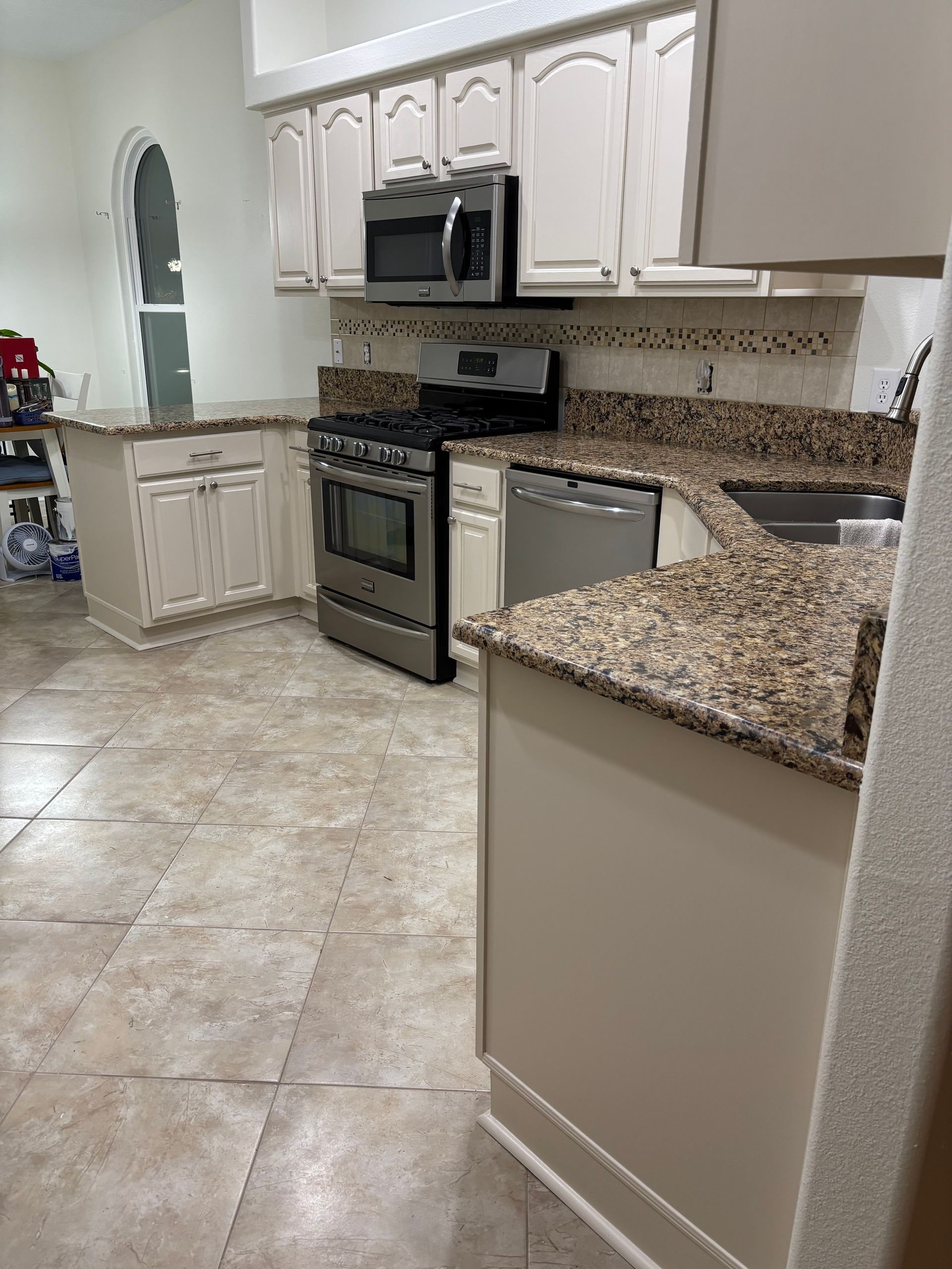 Modern kitchen with white cabinets, stainless steel appliances, and beige tile flooring
