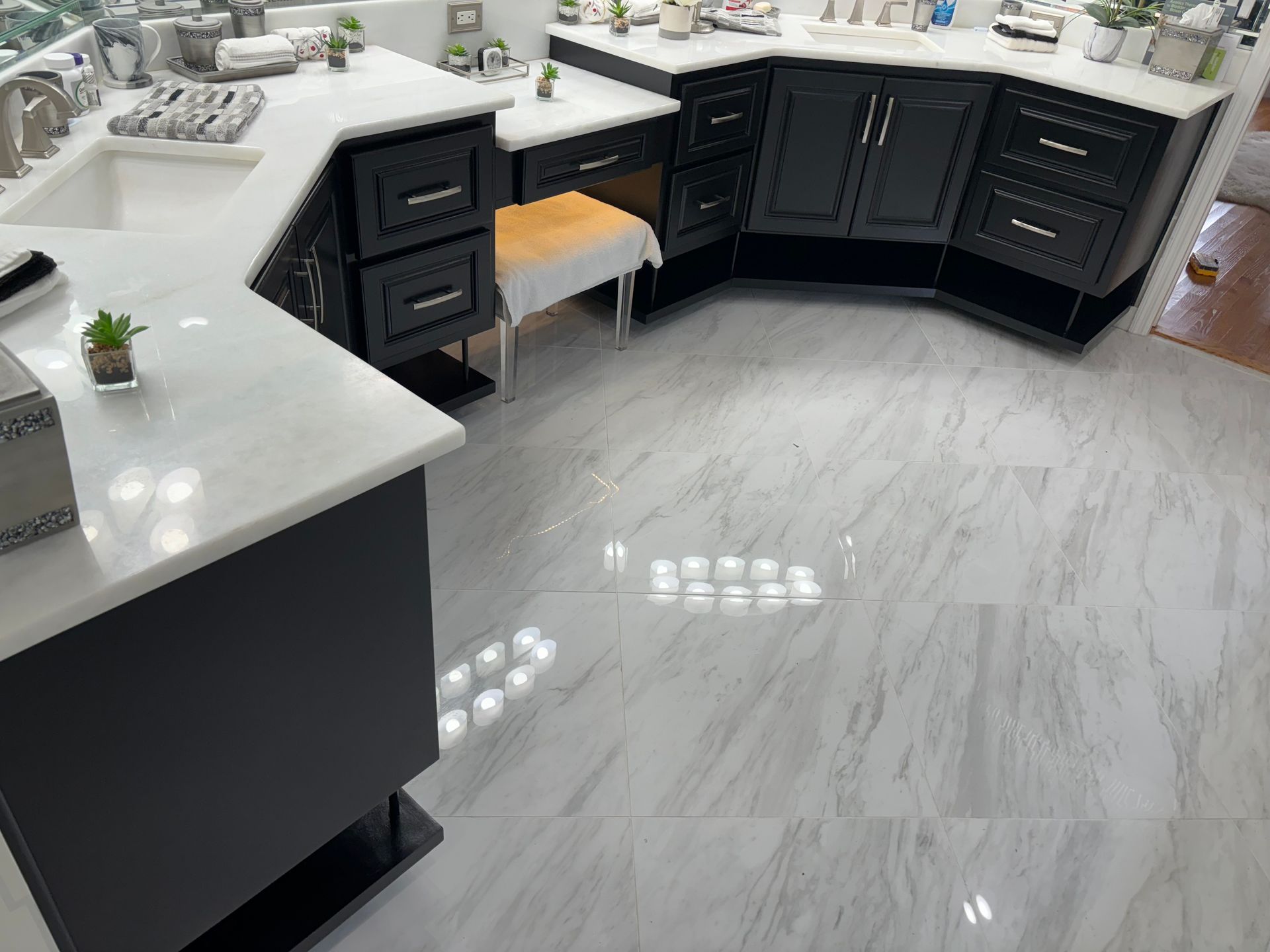 Black and white kitchen with a marble countertop and flooring. A cabinet with drawers and a small stool is near the counter.