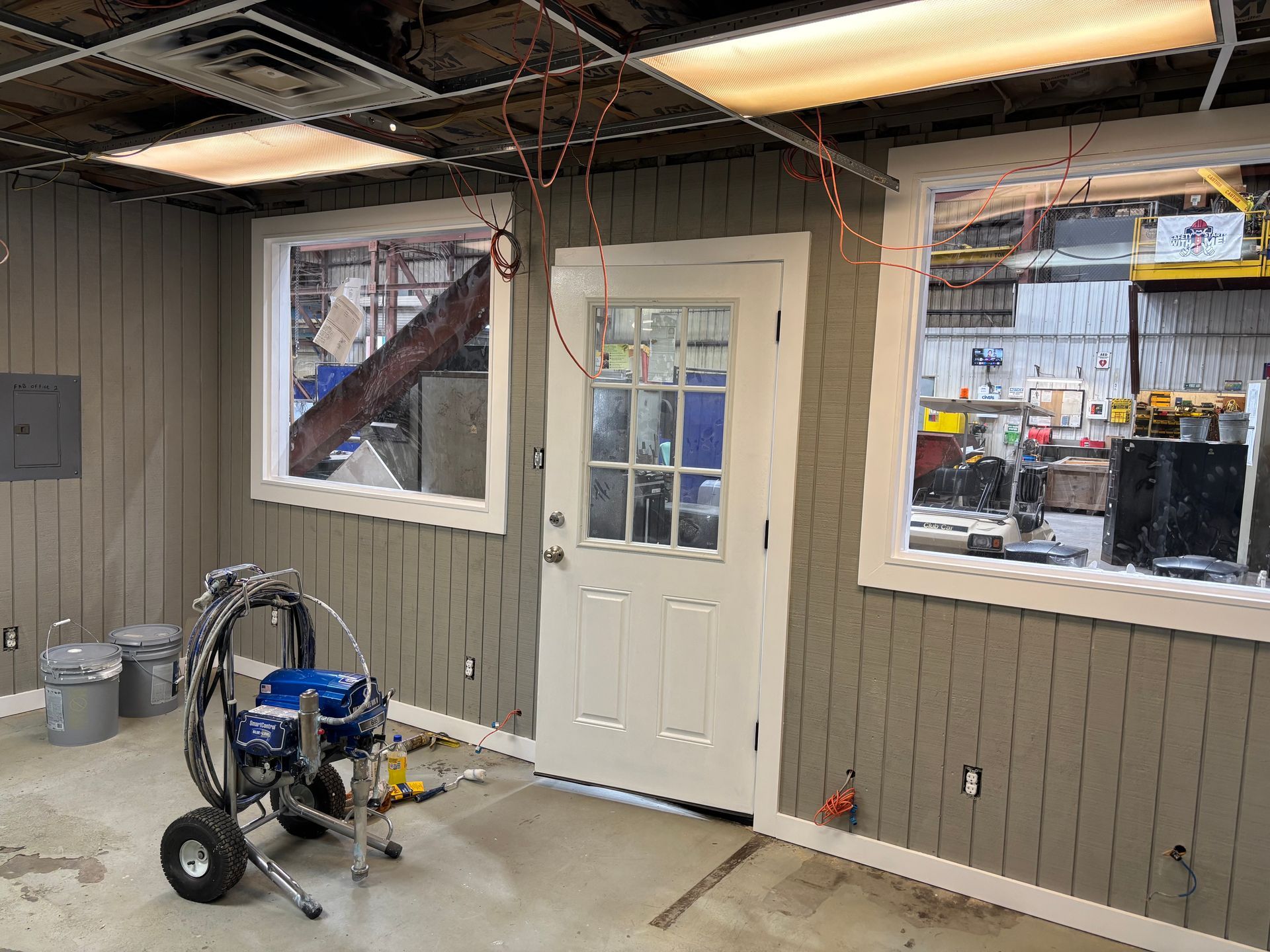 Interior with a white door and windows in a workspace. A paint sprayer sits on the floor.