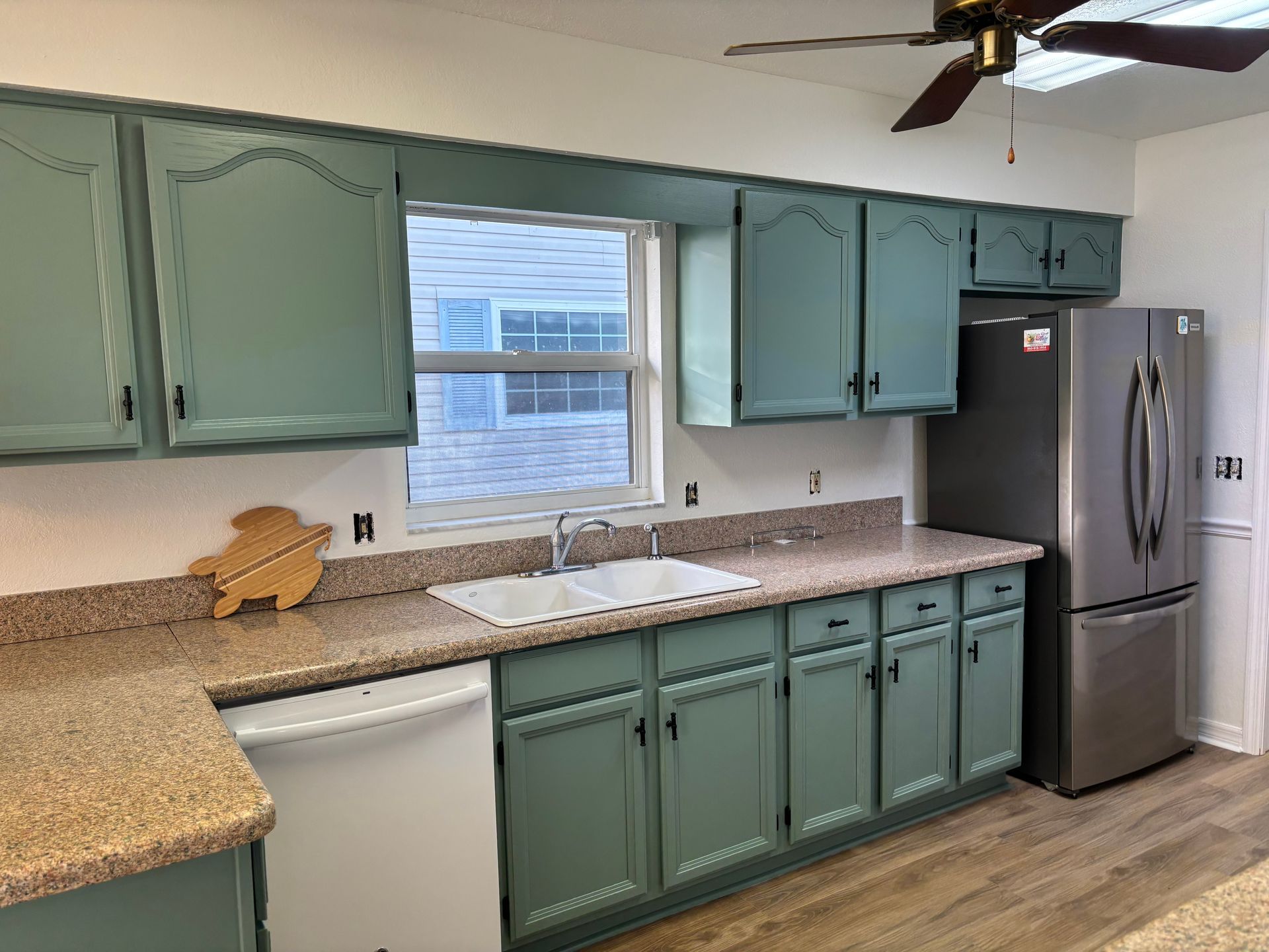 Kitchen with mint green cabinets, speckled countertops, a window over the sink, and a stainless steel refrigerator.