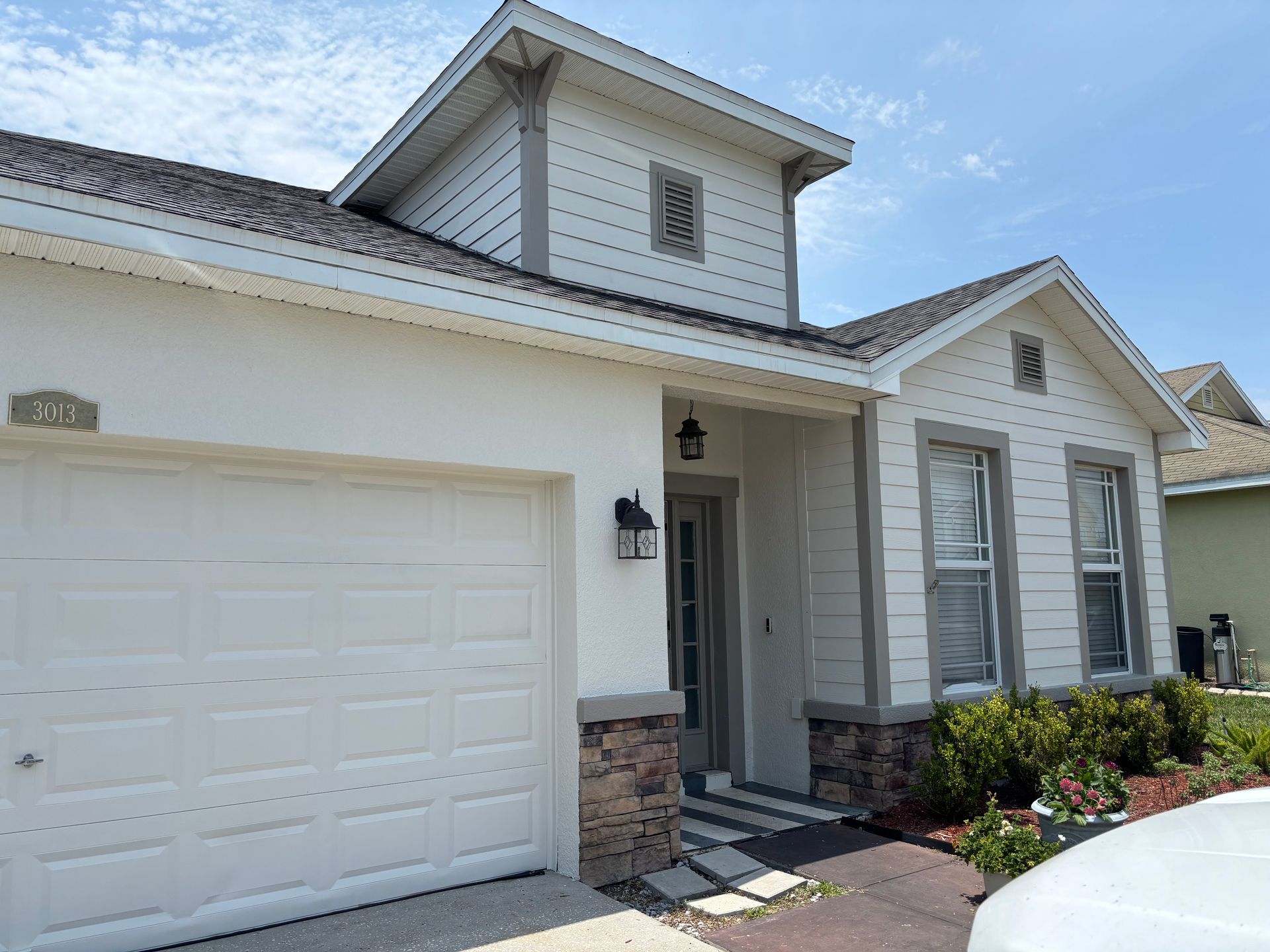 Exterior view of a light beige house with a white garage door and a dark roof against a blue sky.