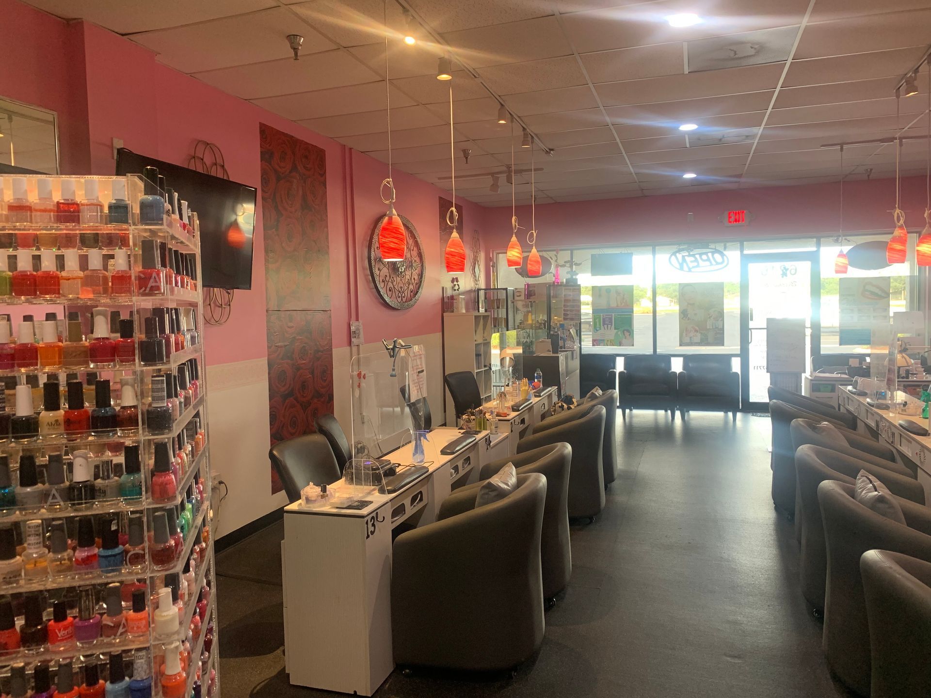 Interior of a nail salon with pink walls, nail polish display, and manicure stations.
