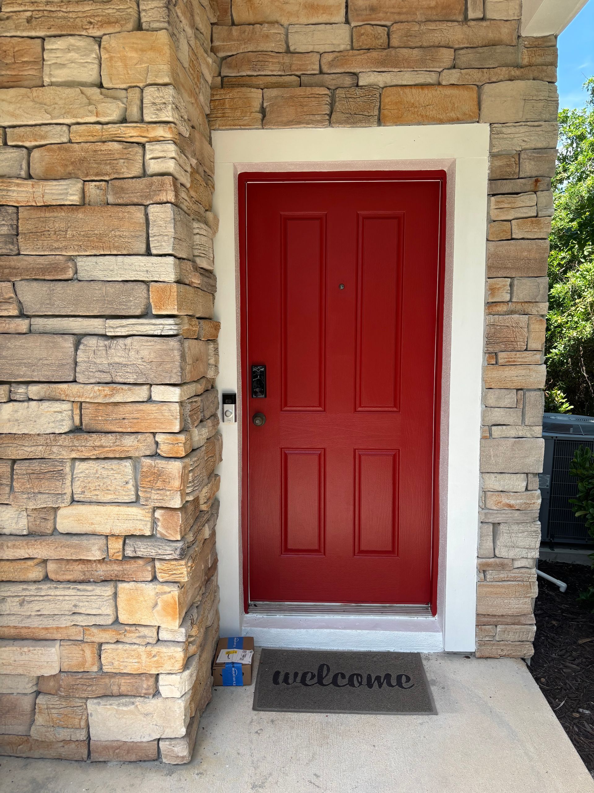 Red front door with stone exterior and doormat by the entrance