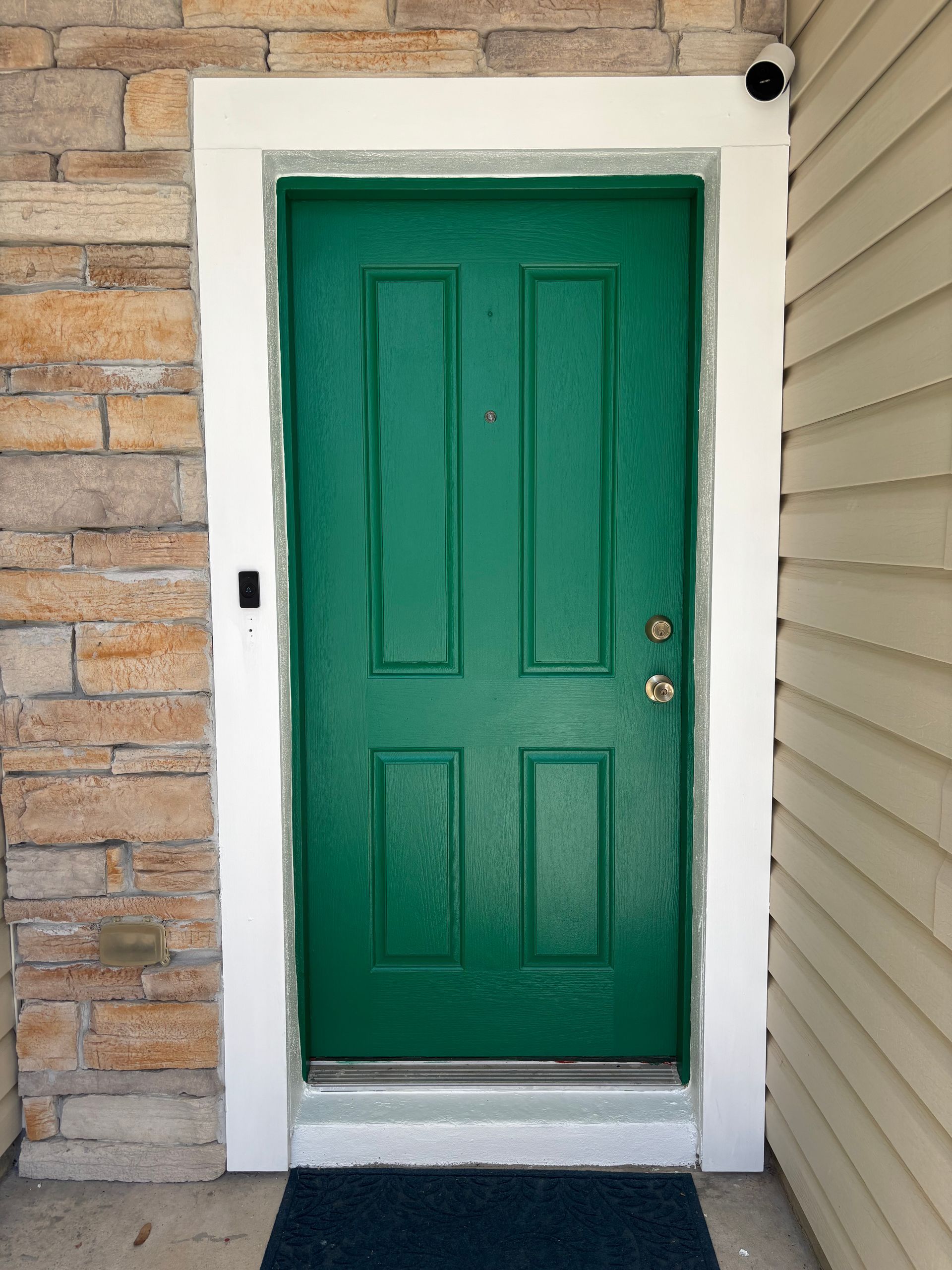 Green front door with white trim and brick siding beside it