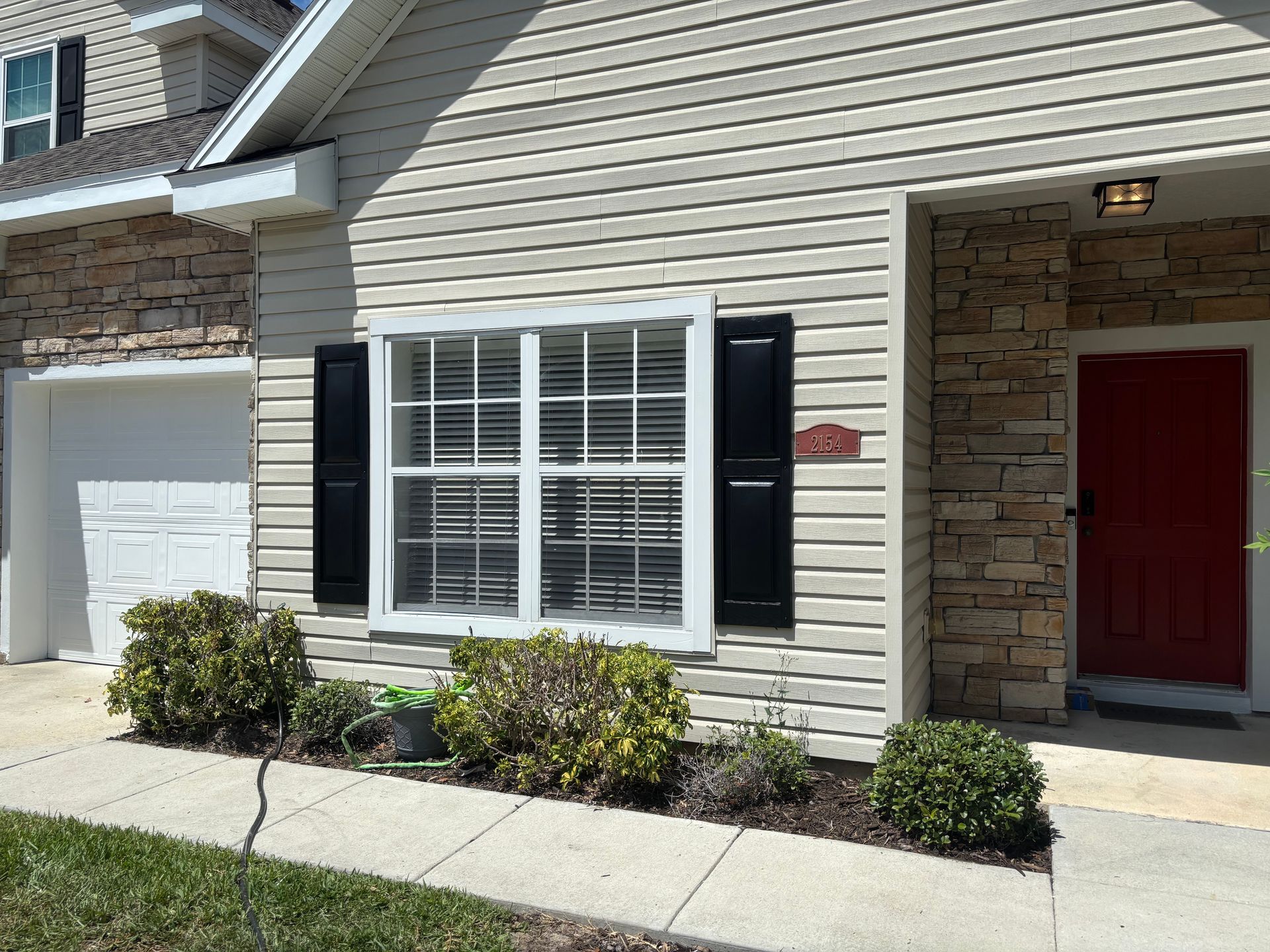 Front of a house with beige siding, white-trimmed window, red front door, and small shrubs by the walkway