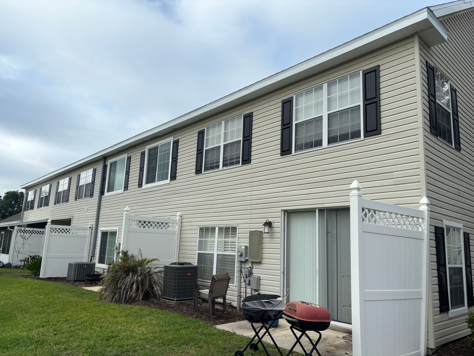 Row of two-story beige townhomes with white trim and small patios under a cloudy sky