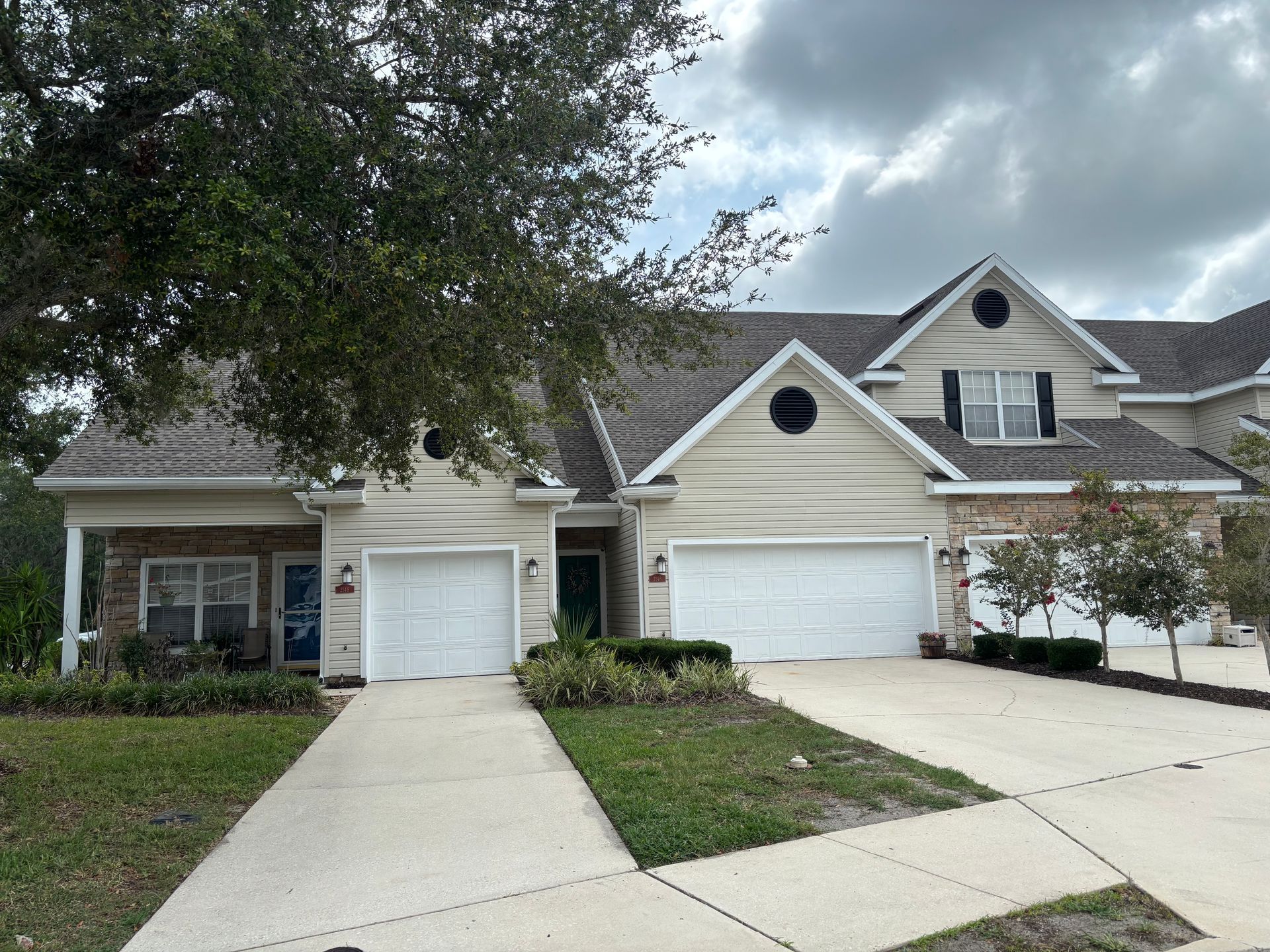 Suburban townhouse with two white garage doors, a driveway, and cloudy sky overhead