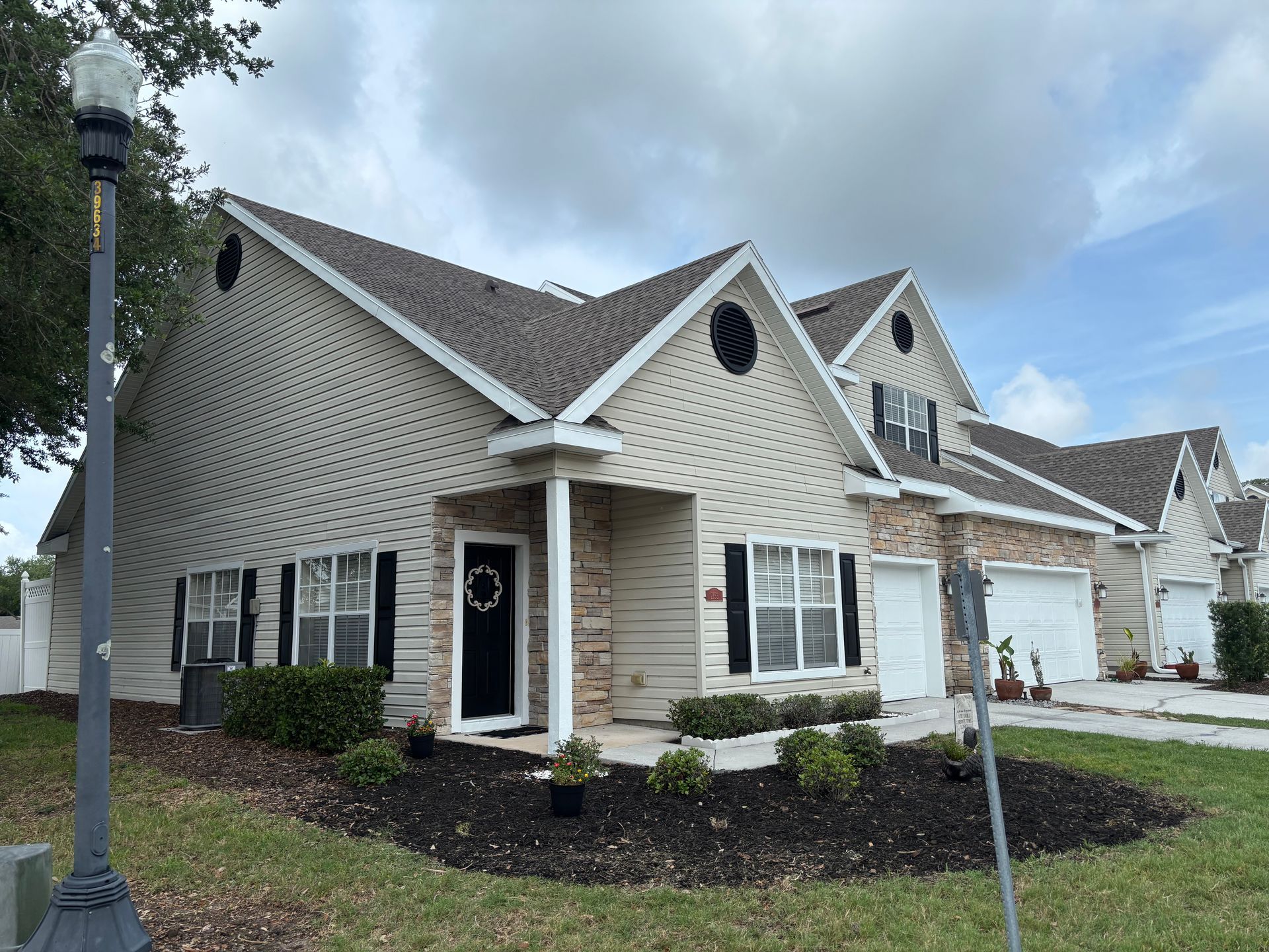 Suburban townhouse with beige siding, white trim, and attached garage under a cloudy sky