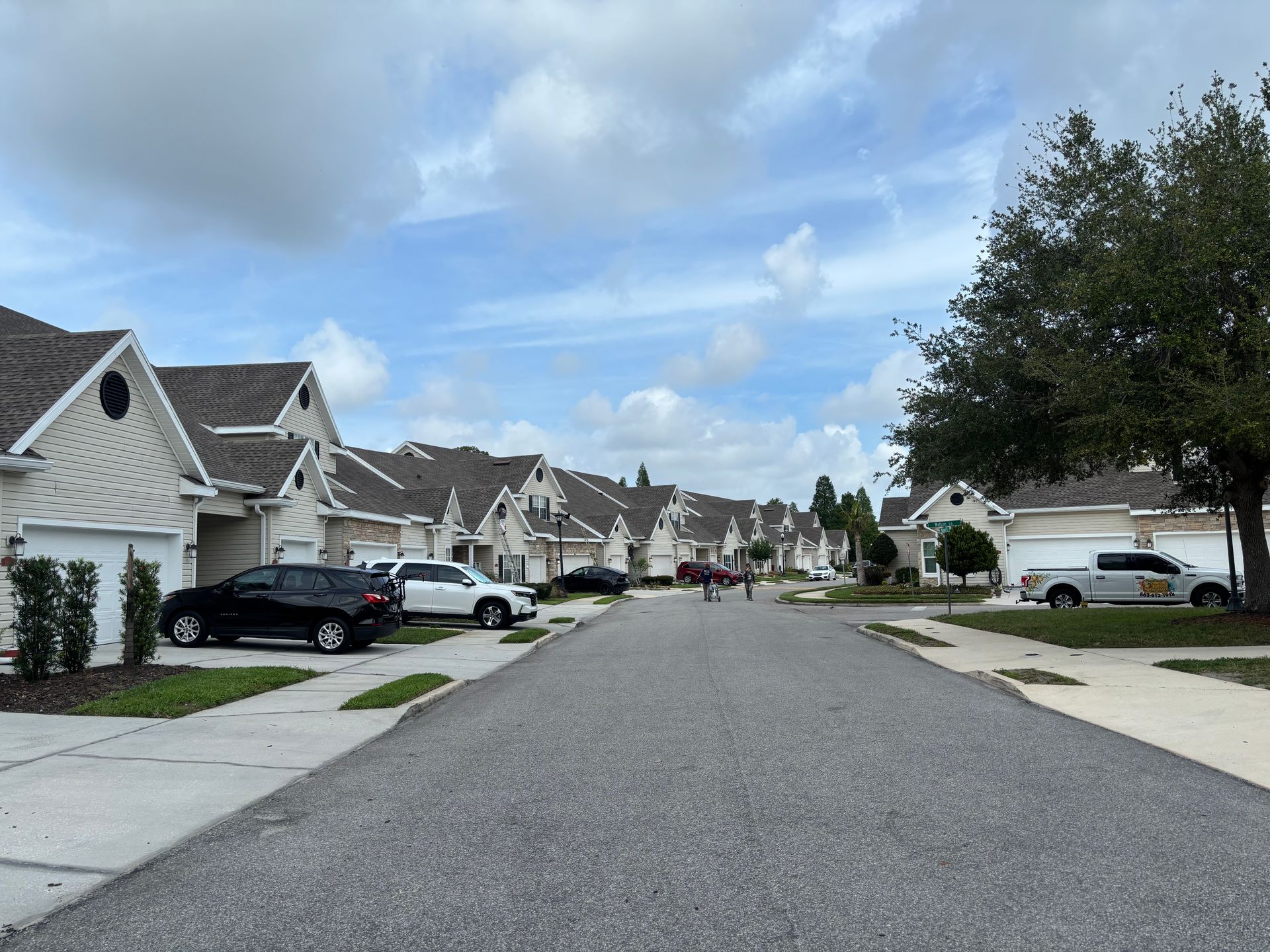 Suburban street with houses, parked cars, and cloudy blue sky