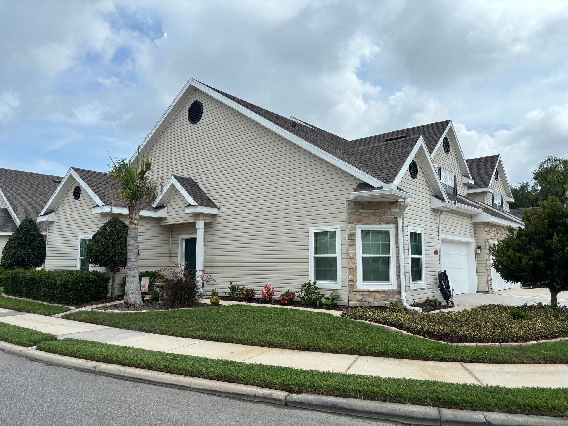Suburban white house with stone siding, manicured lawn, and cloudy sky