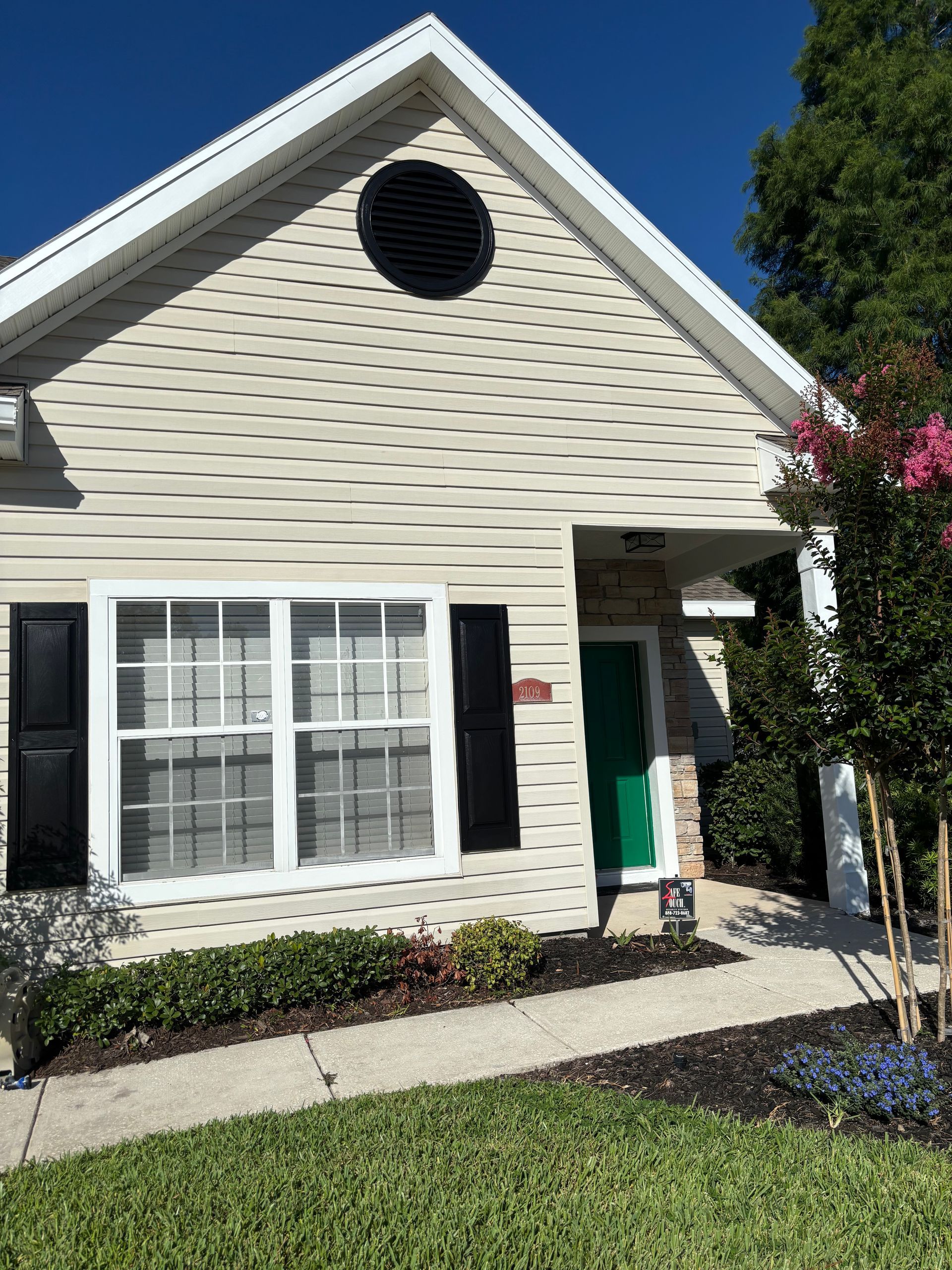 Small beige house with white trim, black shutters, and a front window under a blue sky.