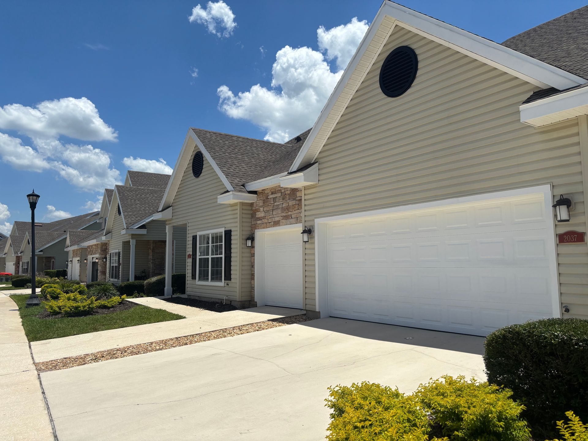 Row of beige suburban houses with white garage doors under a bright blue sky