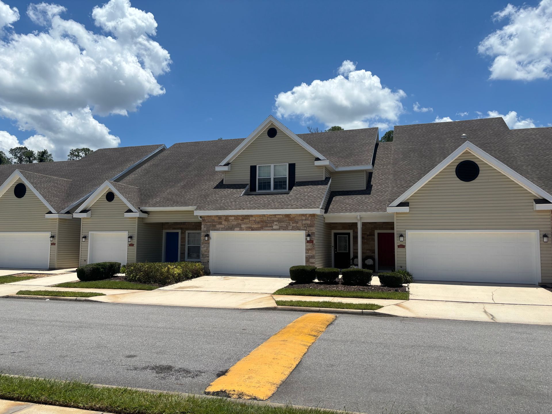 Row of beige suburban townhouses with attached garages under a bright blue sky