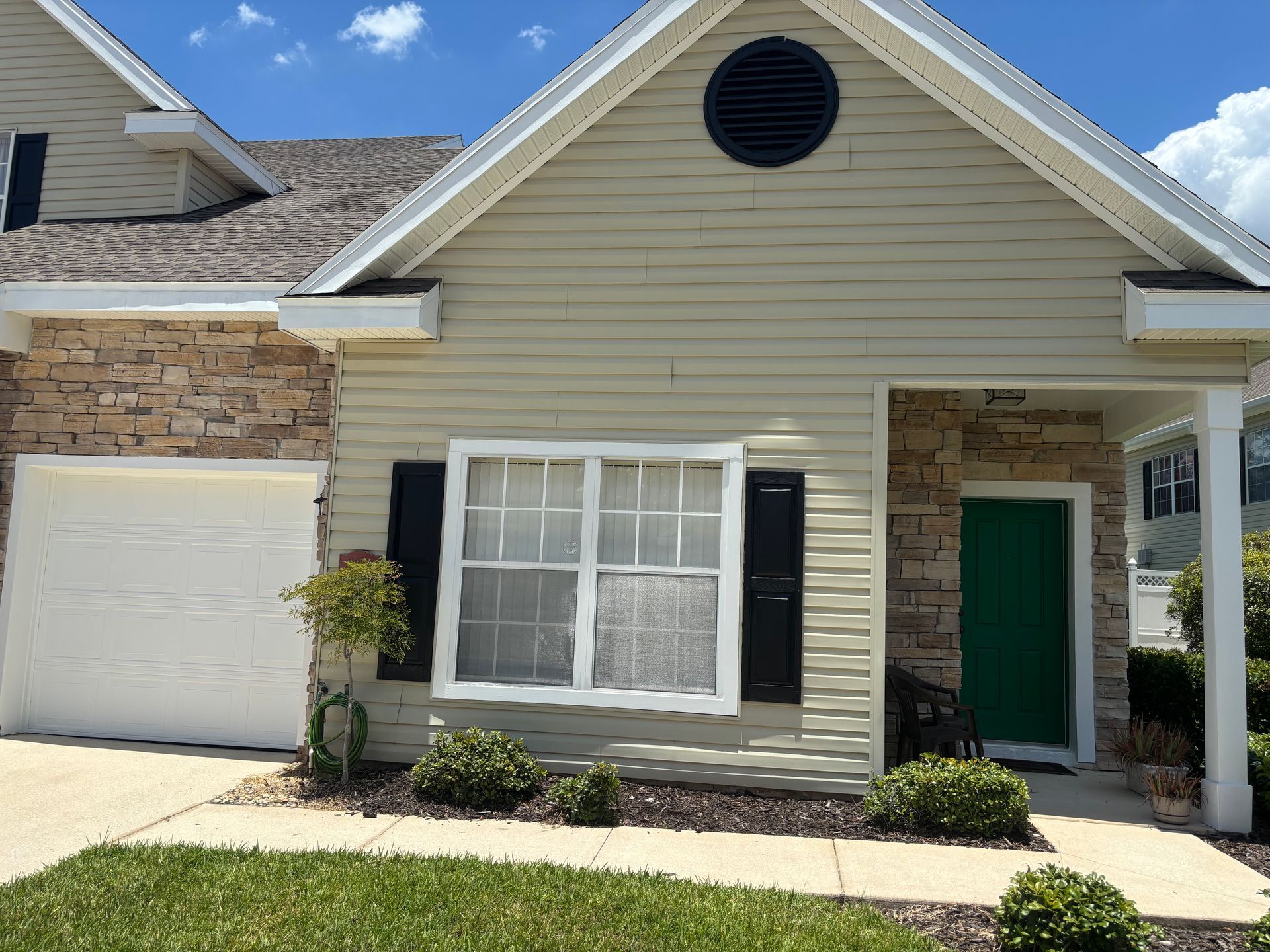 Front of a beige house with white trim, black shutters, a garage, and an open front door