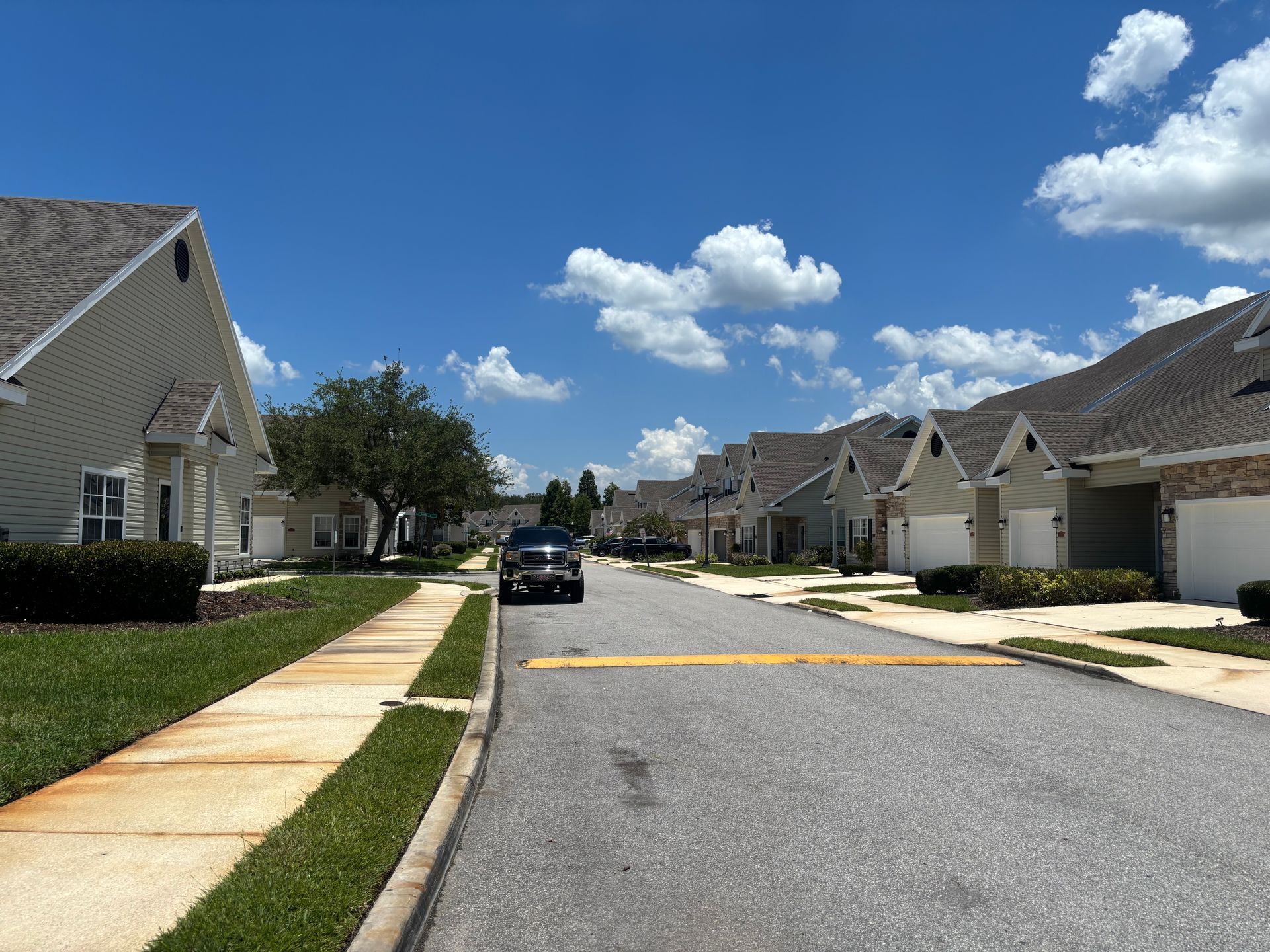 Suburban street with houses, parked car, sidewalks, and a bright blue sky with clouds