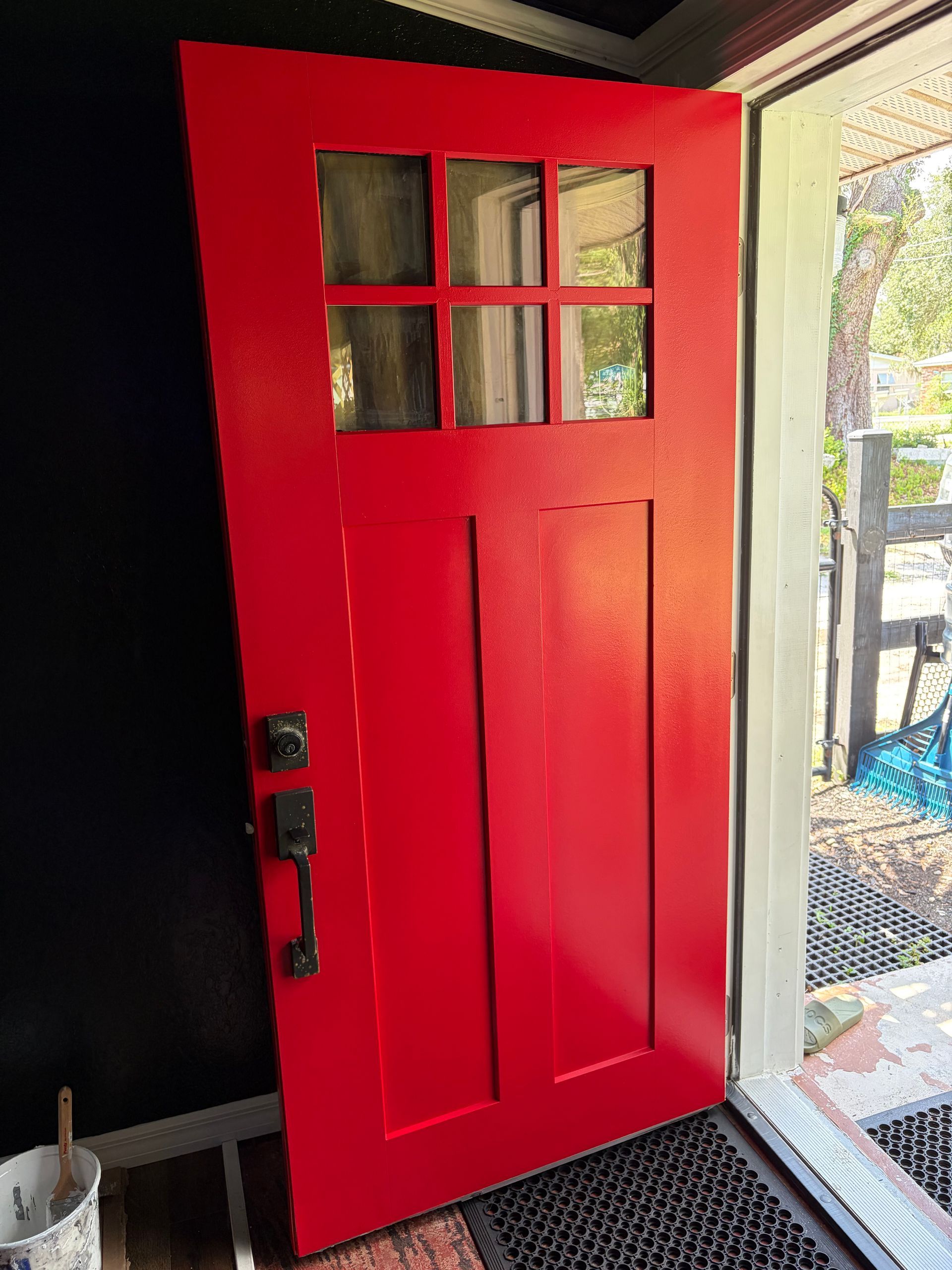 Bright red front door with four glass panes, partly open to a sunlit outdoor patio.