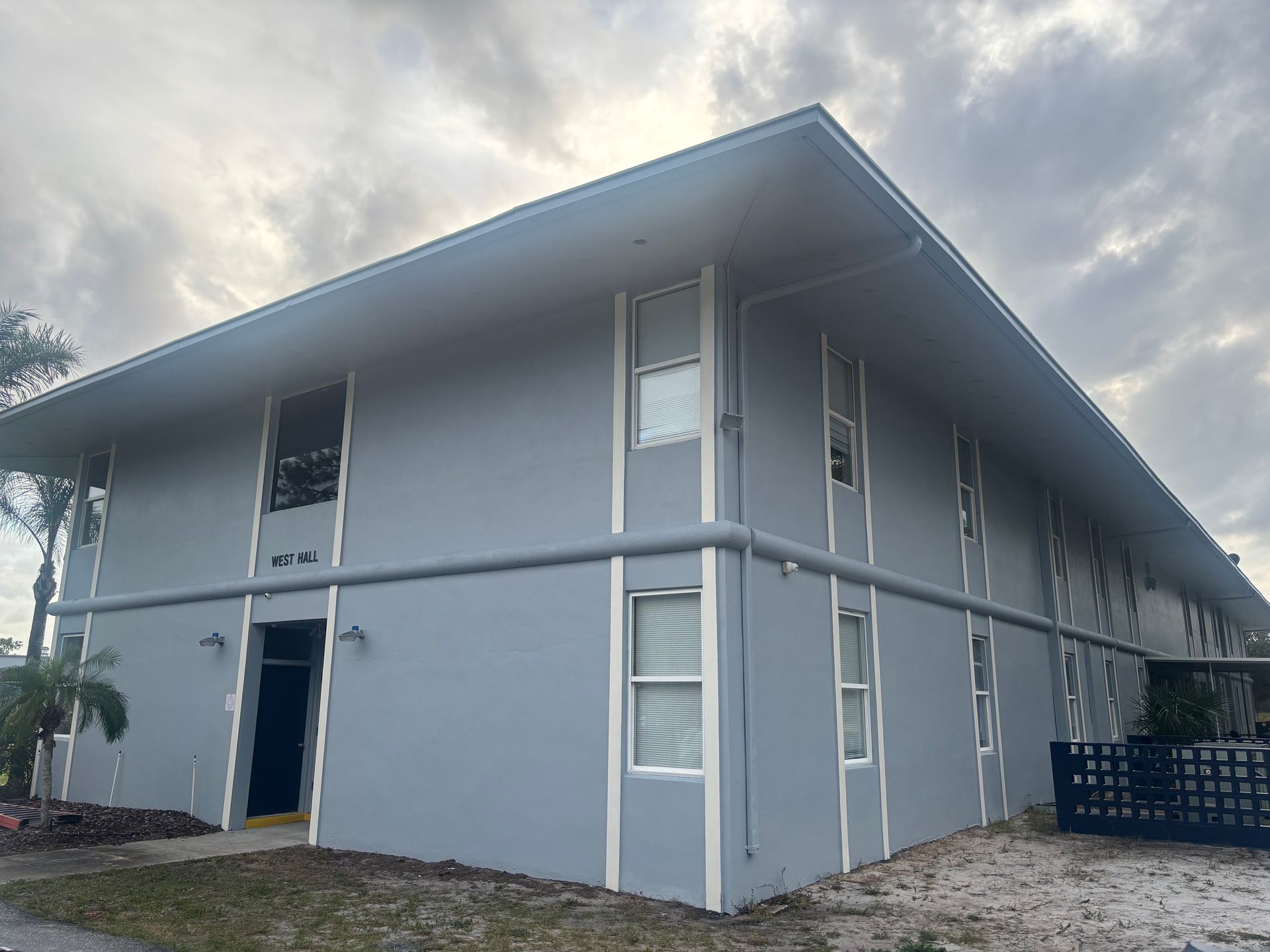 Gray two-story apartment building with white trim under an overcast sky.