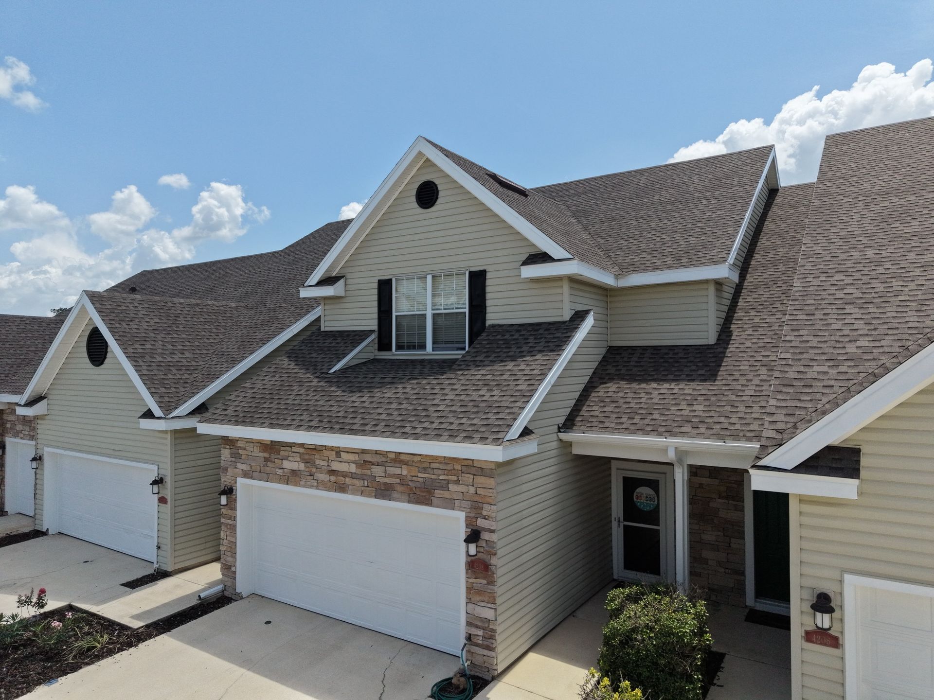 Suburban townhouse row with beige garages, brick accents, and a clear blue sky