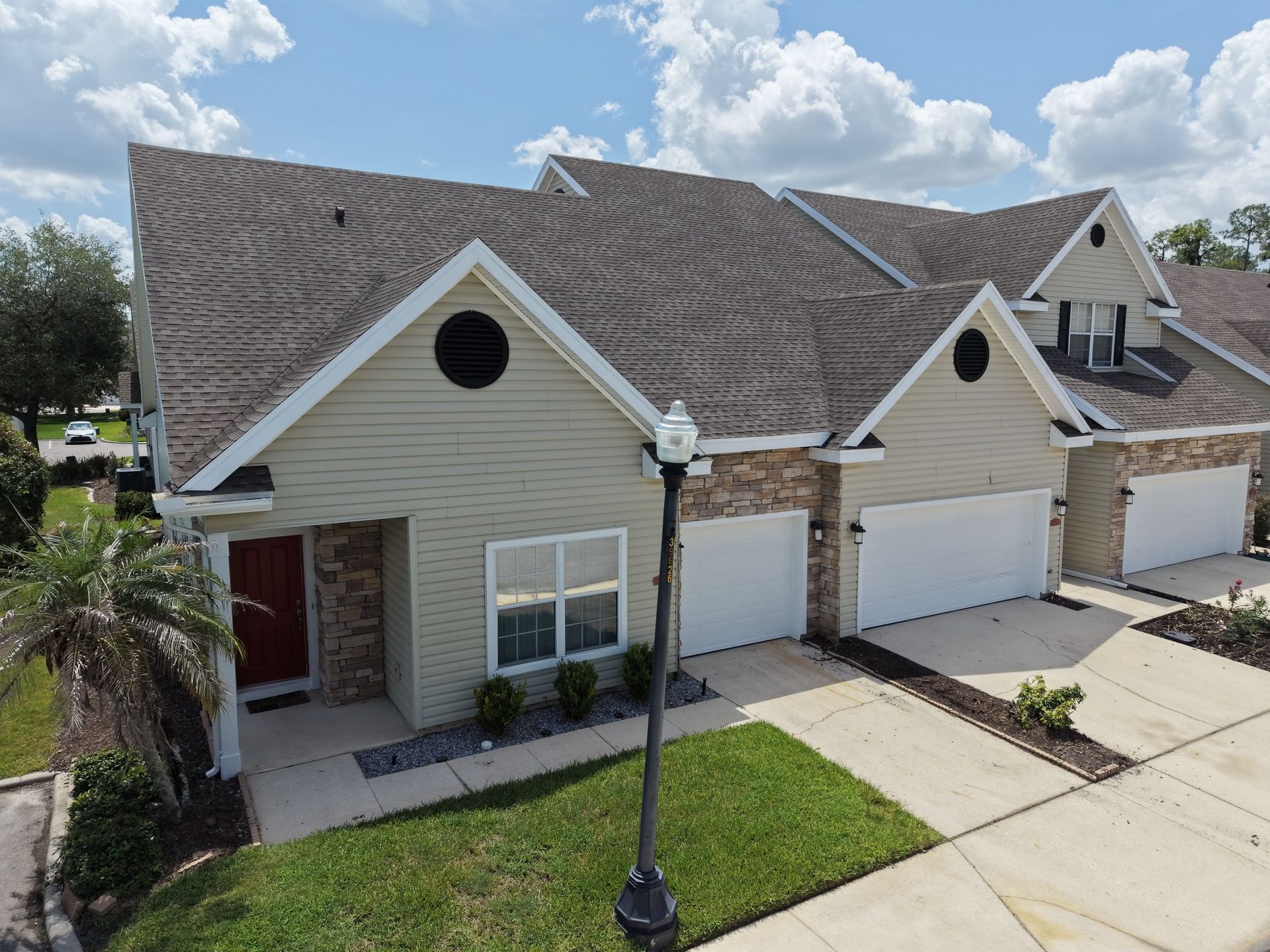 Suburban townhouse exterior with tan siding, two white garage doors, a front lawn, and a lamppost