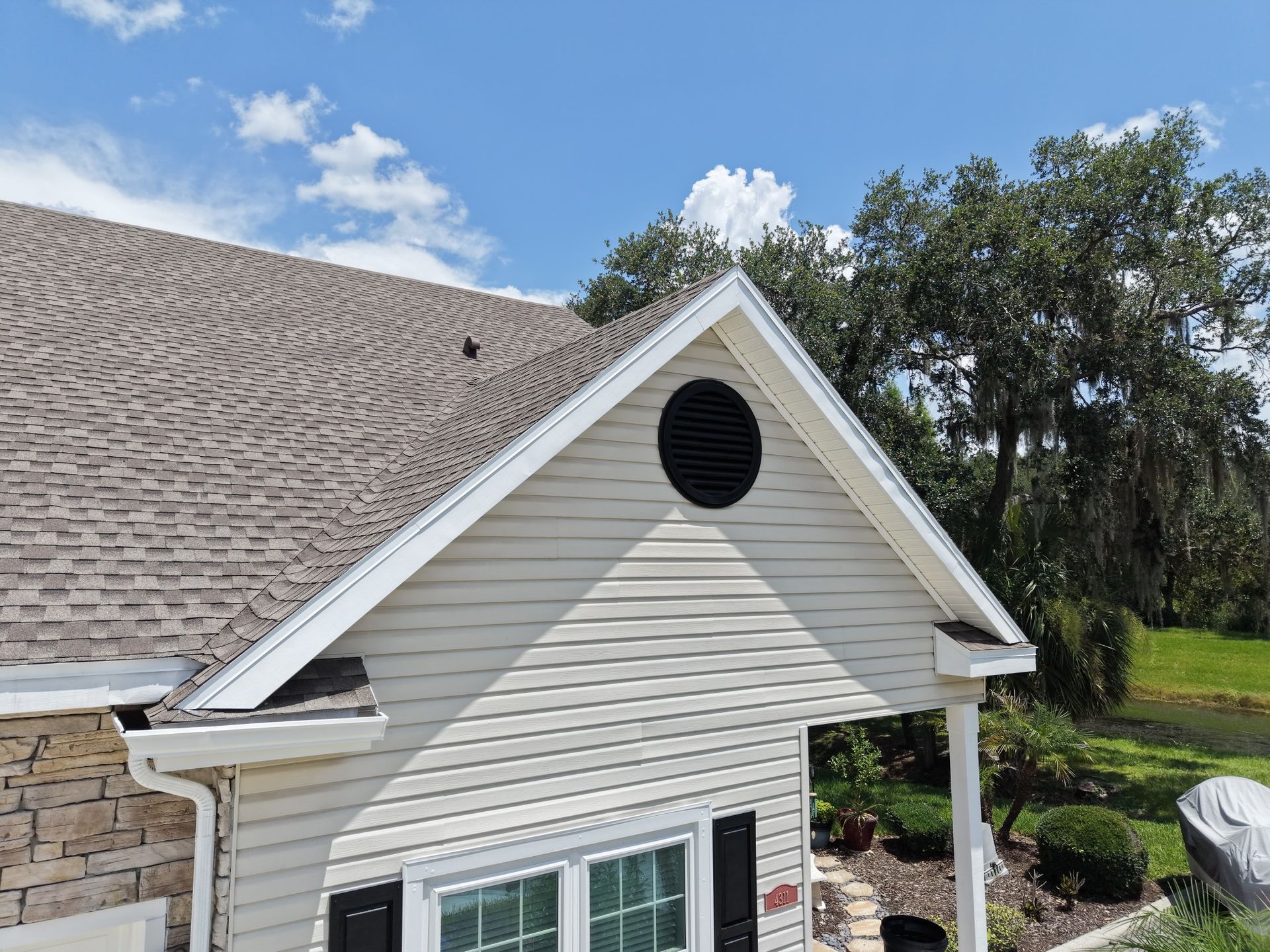 House exterior with tan siding, white trim, and a steep gabled roof under a blue sky