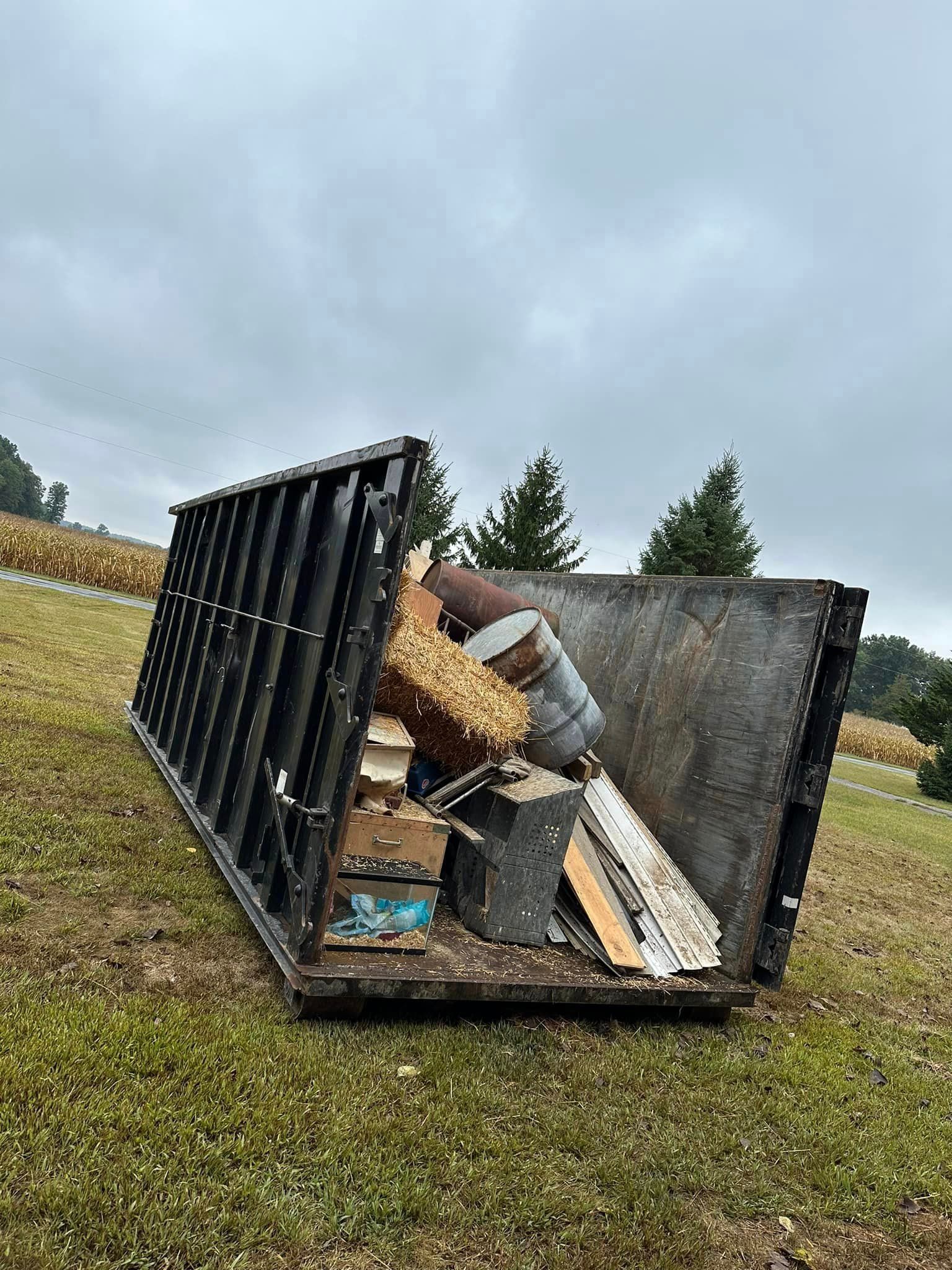 A dumpster filled with junk is sitting on top of a lush green field.