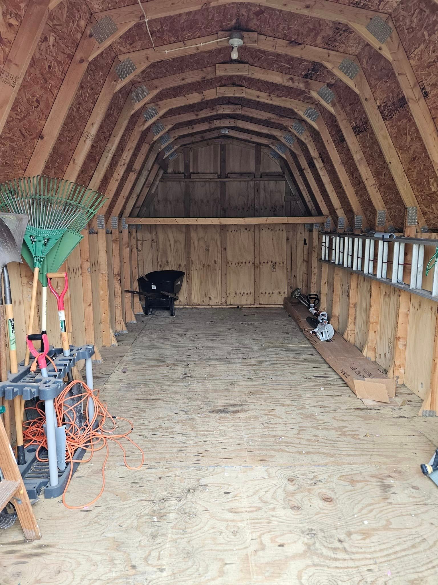 The inside of a wooden barn filled with tools and a dog.