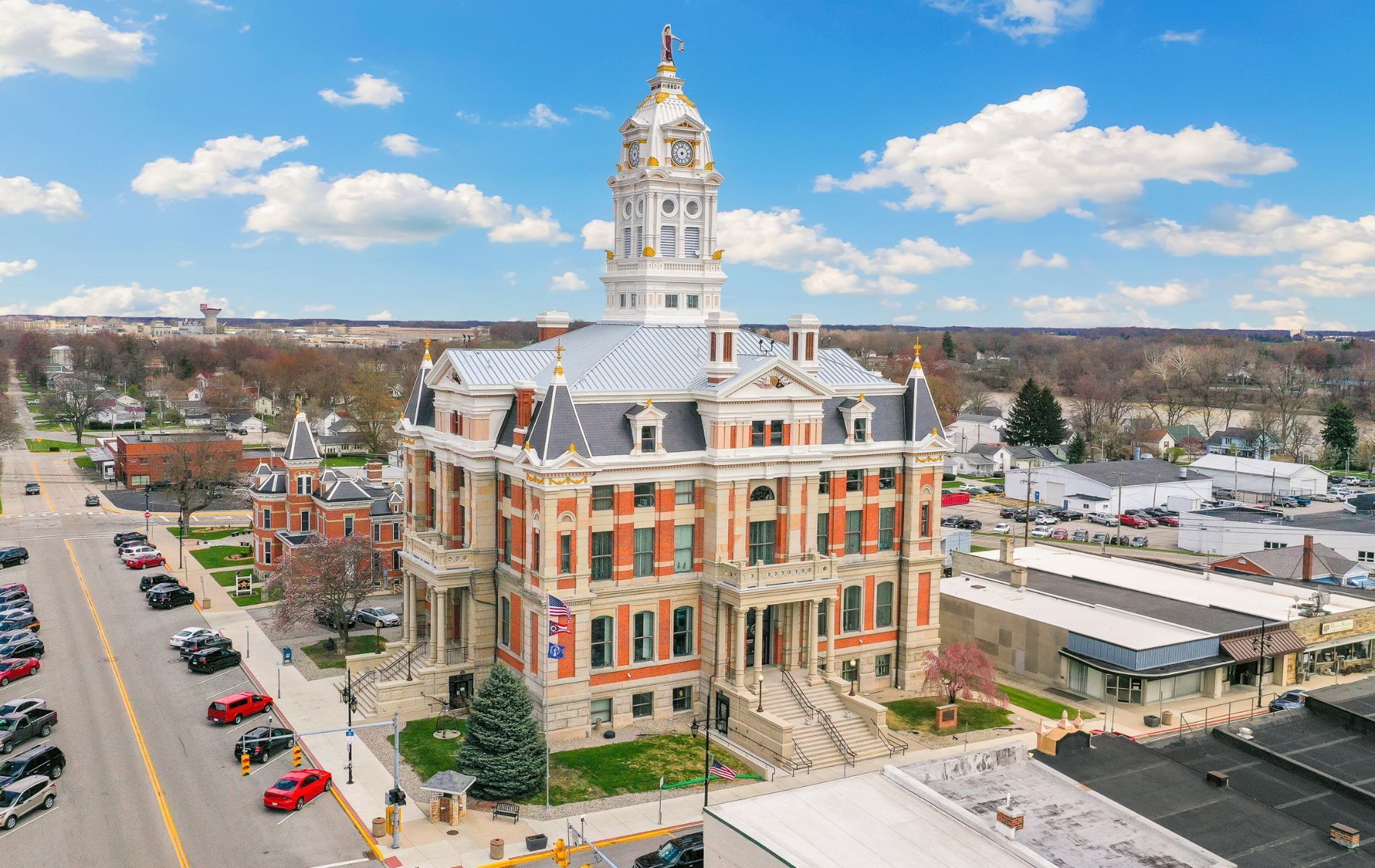 An aerial view of a courthouse in a small town with cars parked in front of it.
