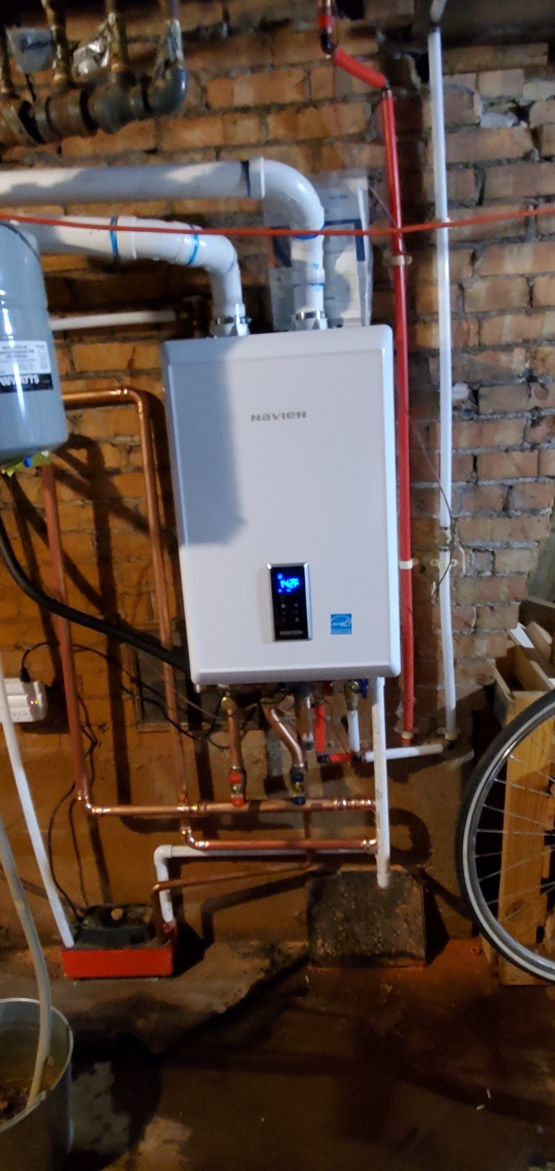 A water heater is installed in a basement next to a bicycle.