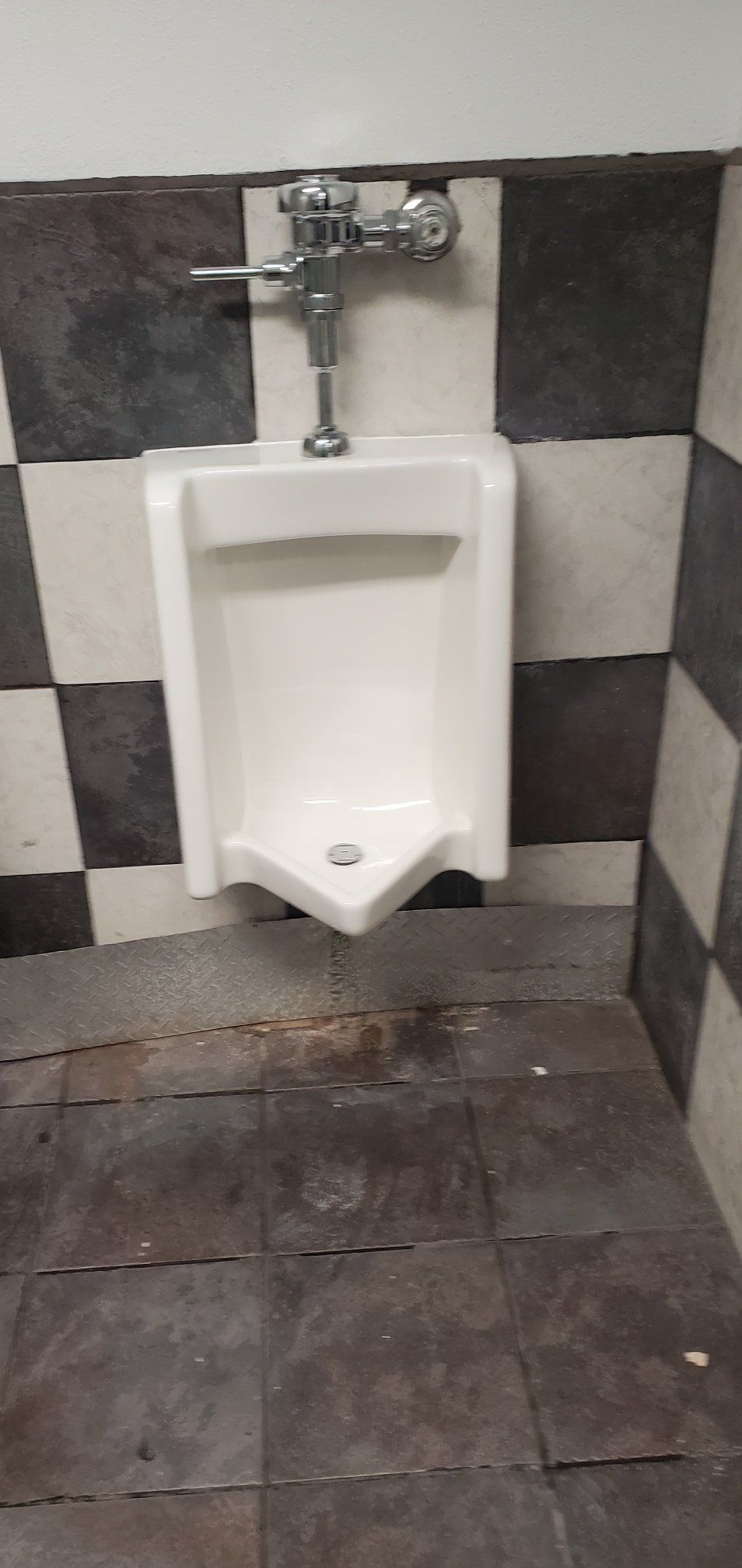 A white urinal is sitting in a bathroom next to a checkered wall.