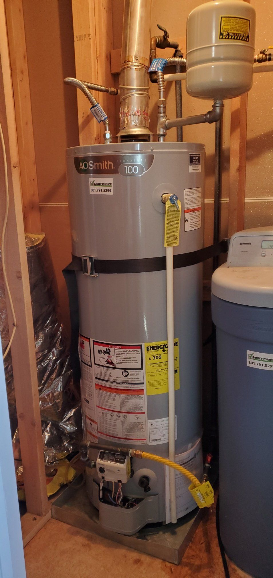 A water heater is sitting in a room next to a washer and dryer.