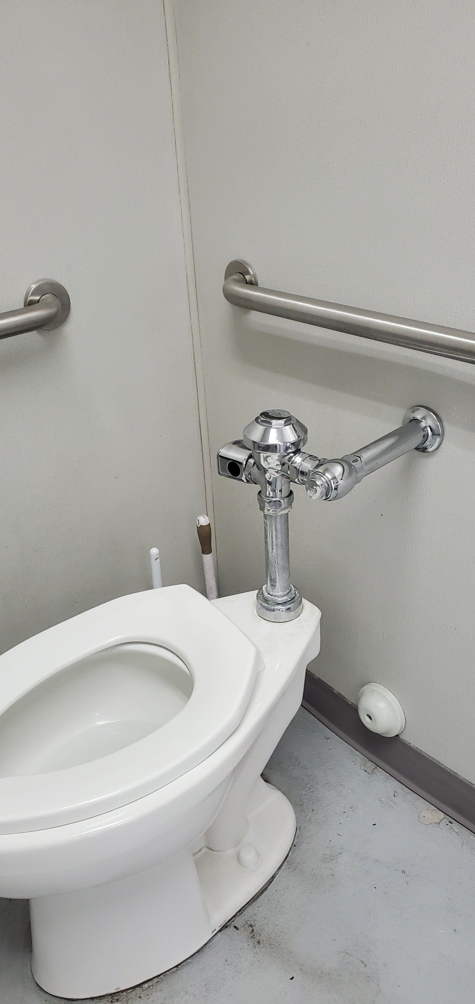 A white toilet is sitting in a bathroom next to a stainless steel railing.
