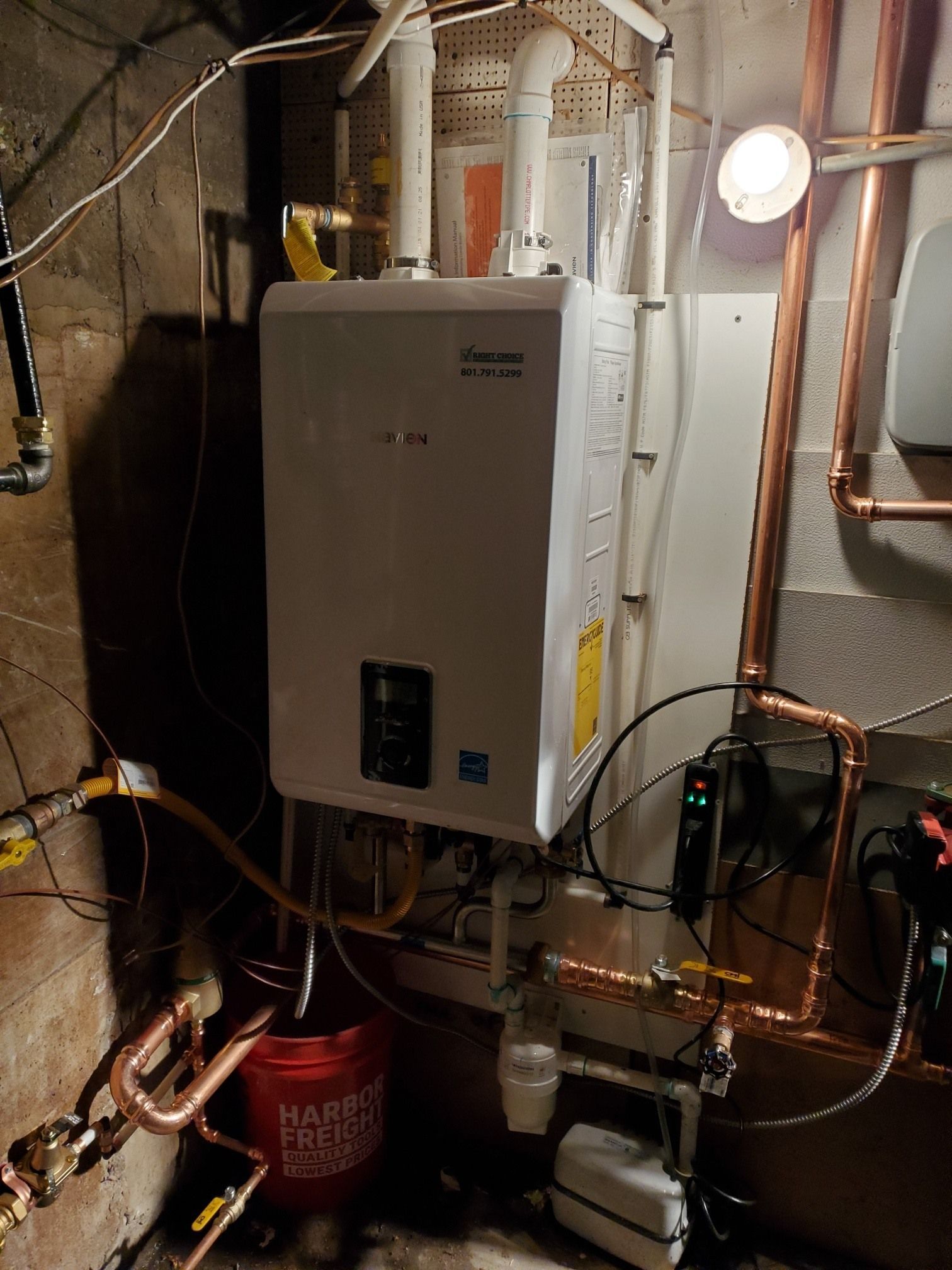 A water heater is sitting in a basement next to copper pipes.